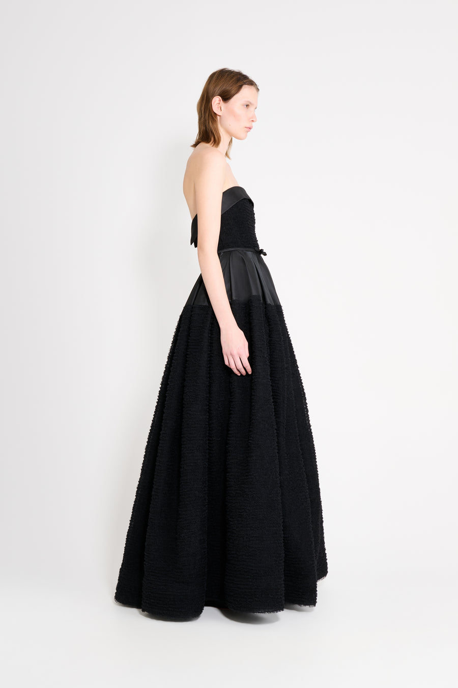 Model wearing a black strapless gown from the side.