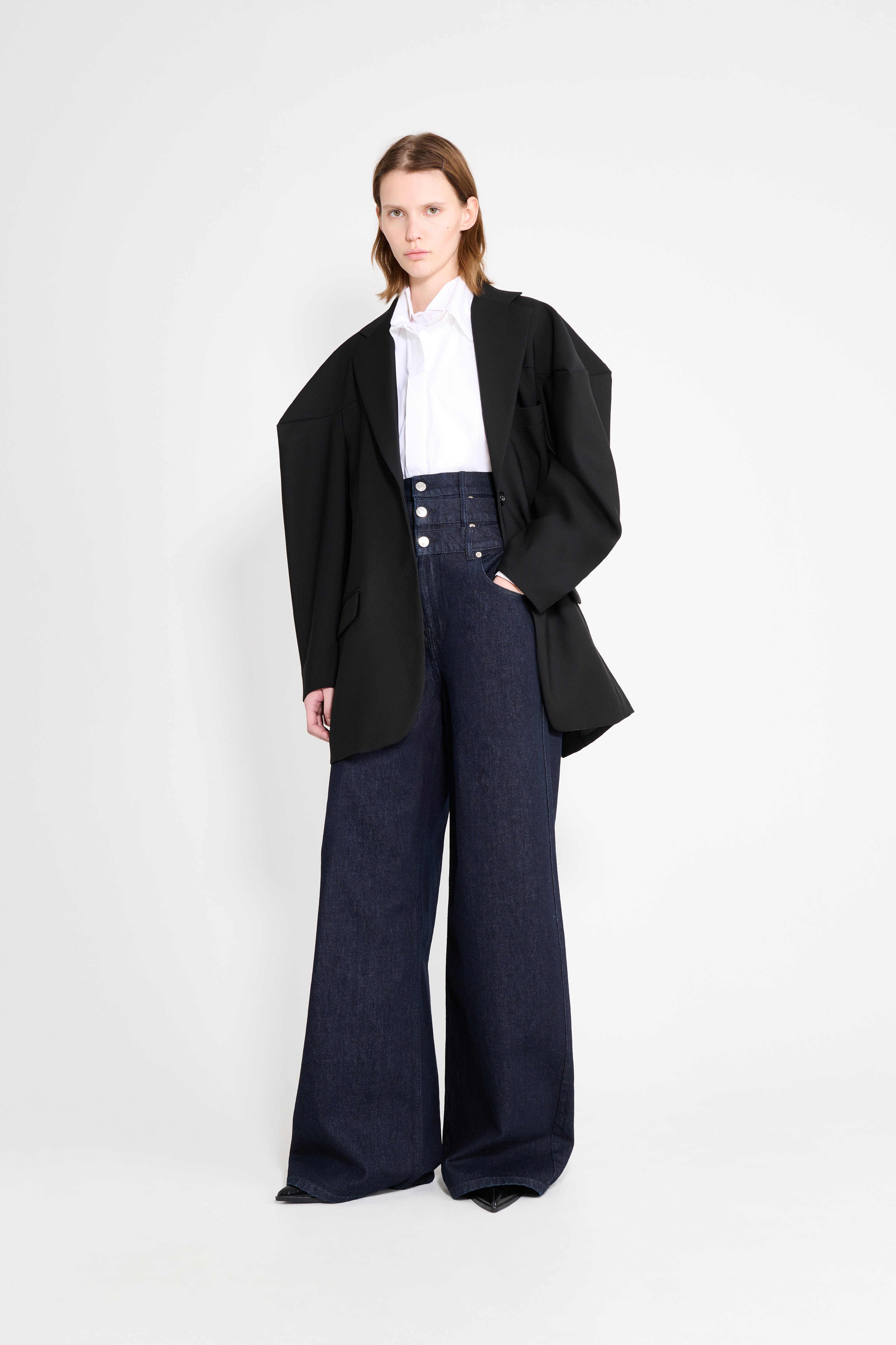 Model wearing a black square blazer with denim pants on a white background.