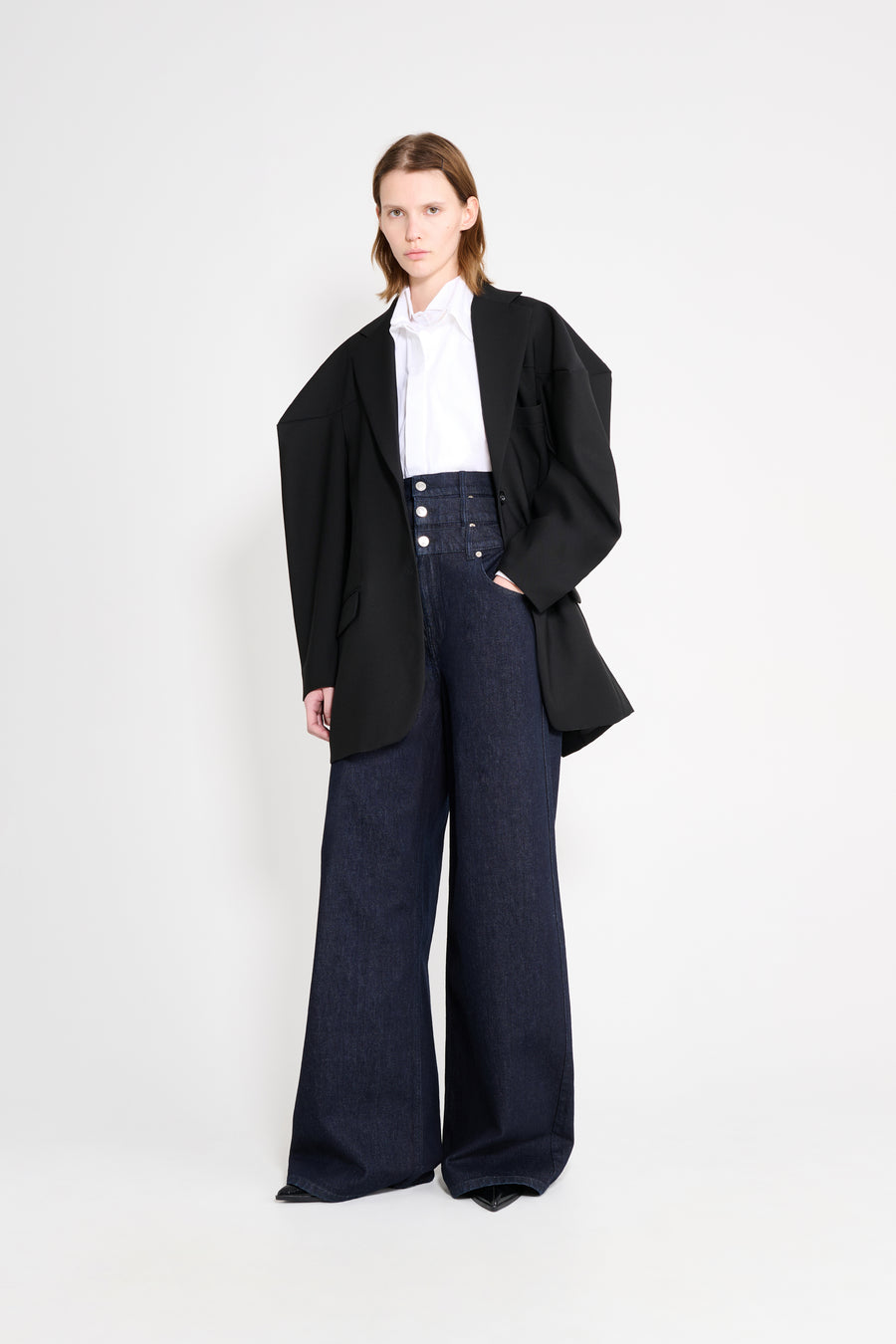 Model wearing a black square blazer with denim pants on a white background.