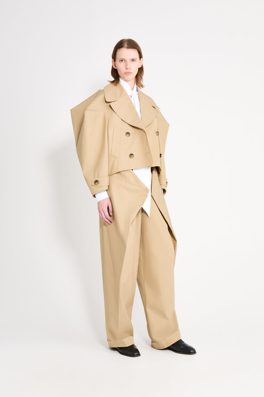 Person wearing a beige trench coat and pants on a white background