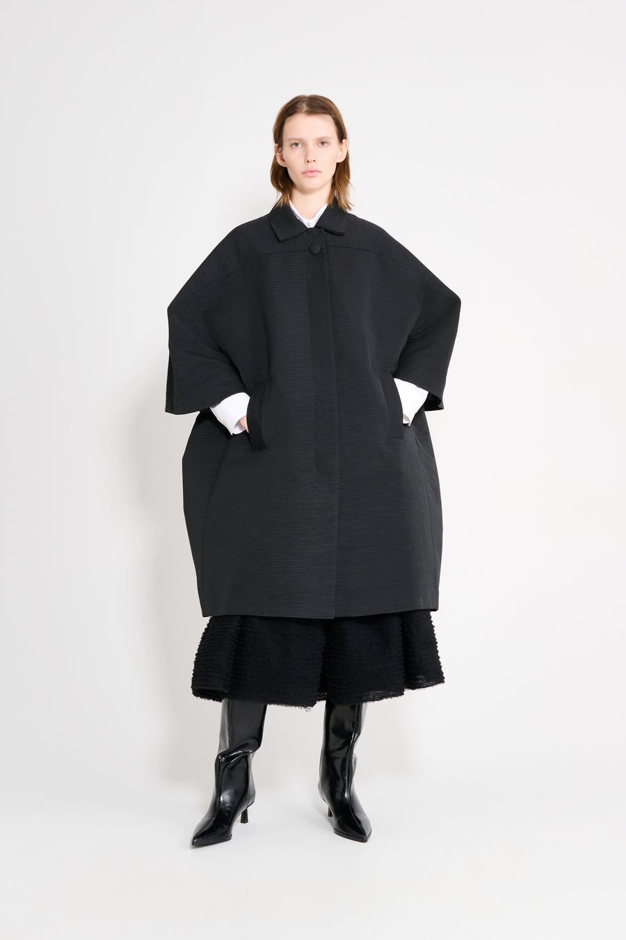 Model wearing a black square coat on a white background.