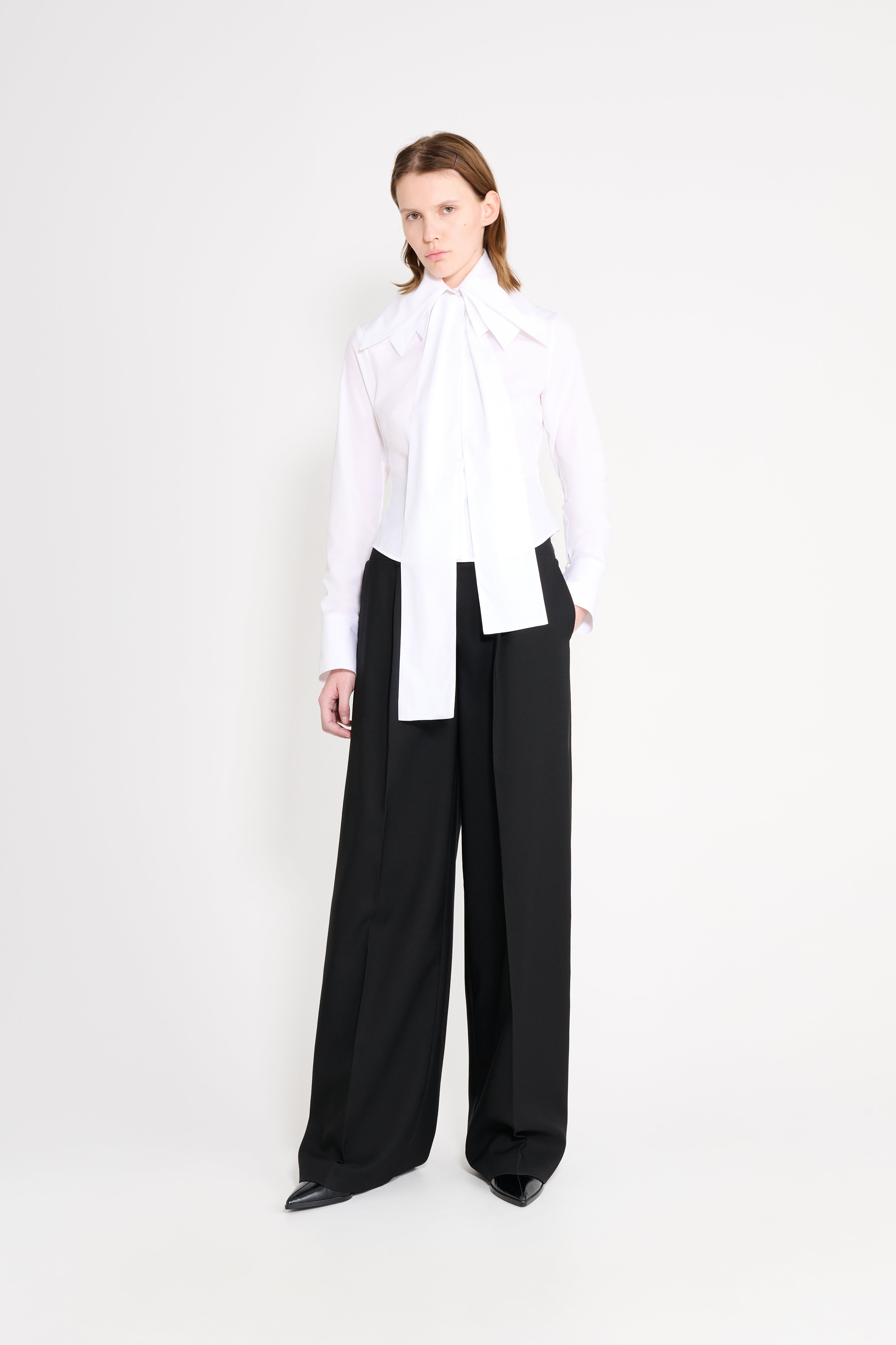 Person wearing a white blouse and black pants on a white background