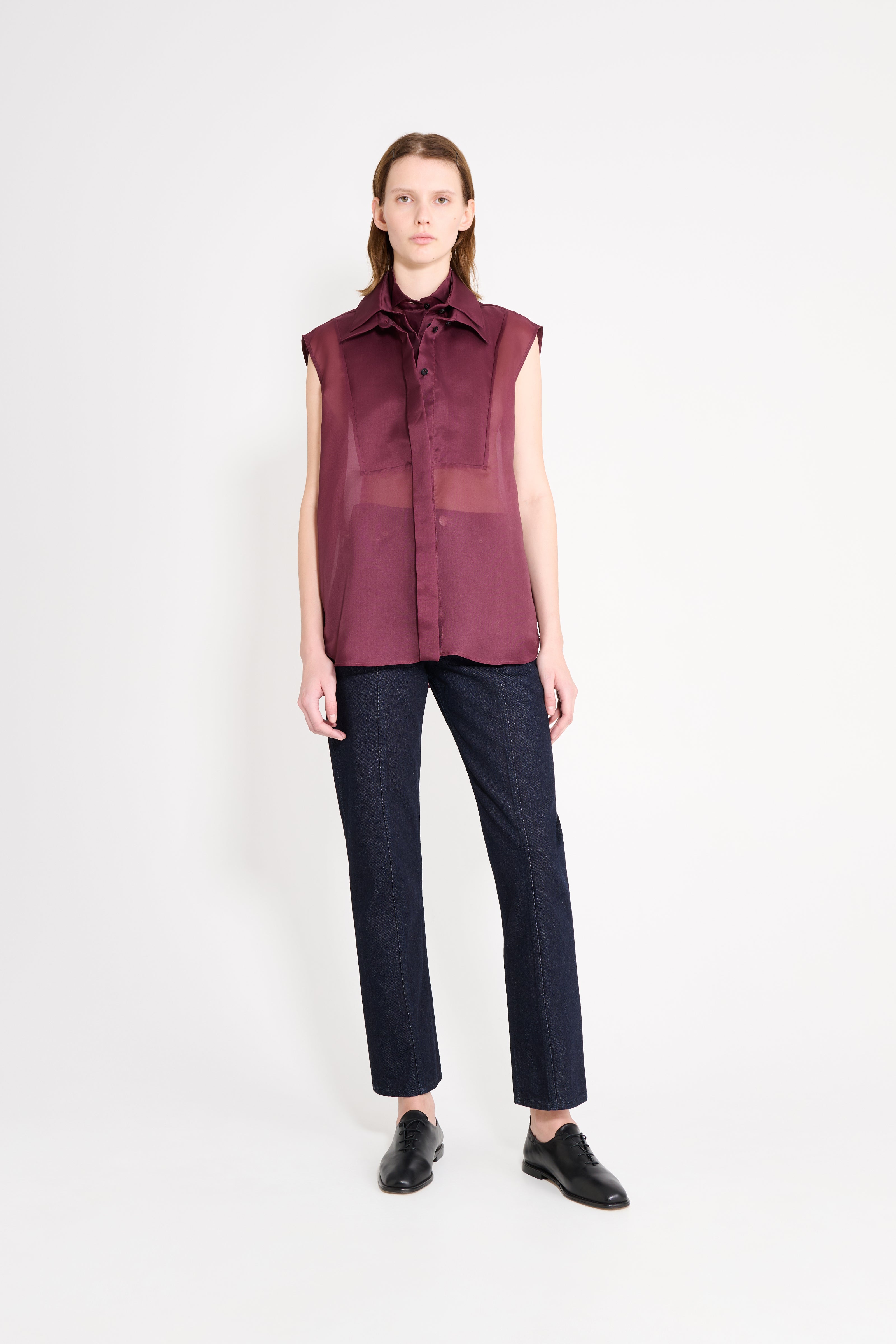 Model wearing a burgundy shirt with dark denim straight leg pants on a white background.