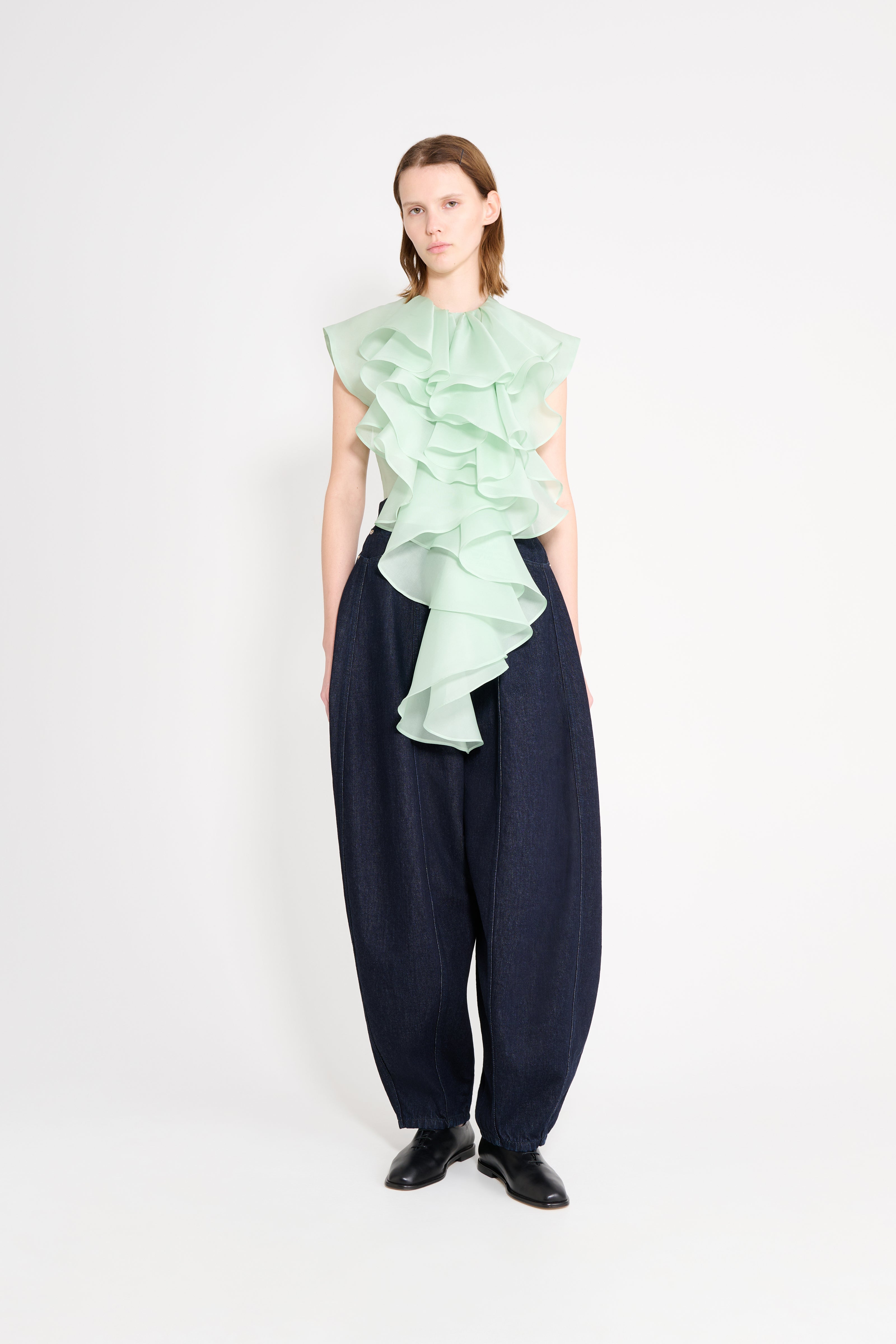 Model wearing a light green ruffled top and dark blue pants on a white background