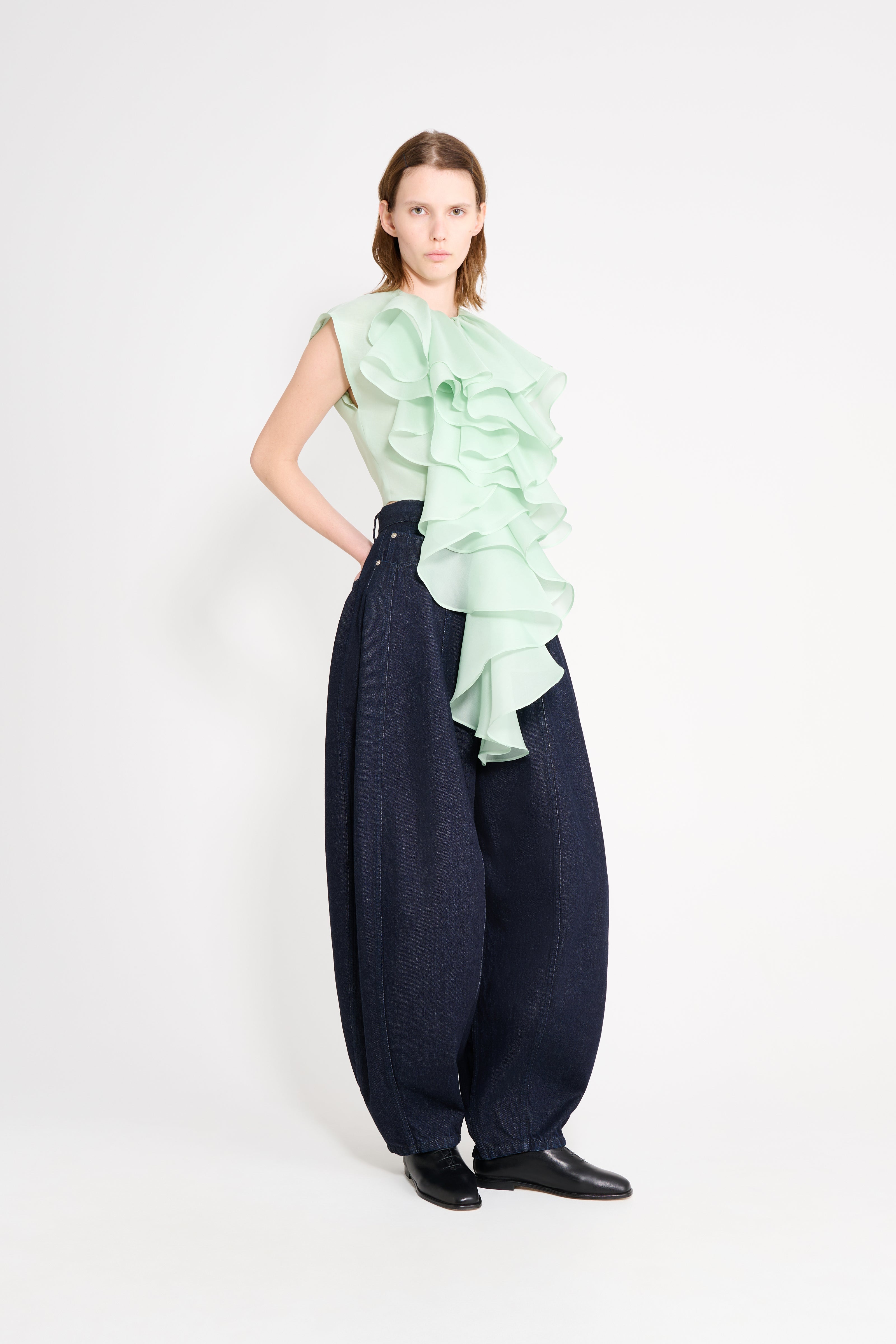 Woman wearing a light green ruffled top and navy wide-leg pants on a white background