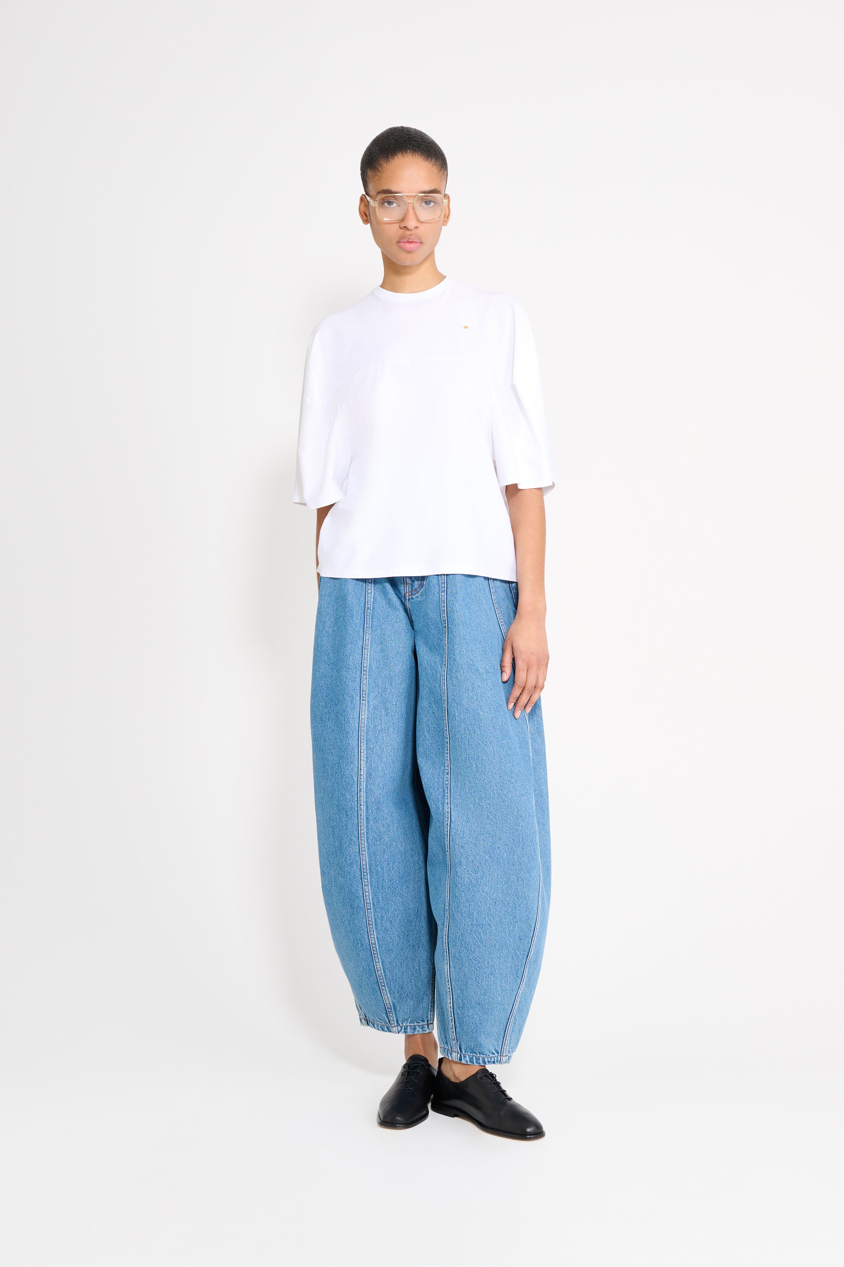 Person wearing a white oversized t-shirt and blue jeans on a white background