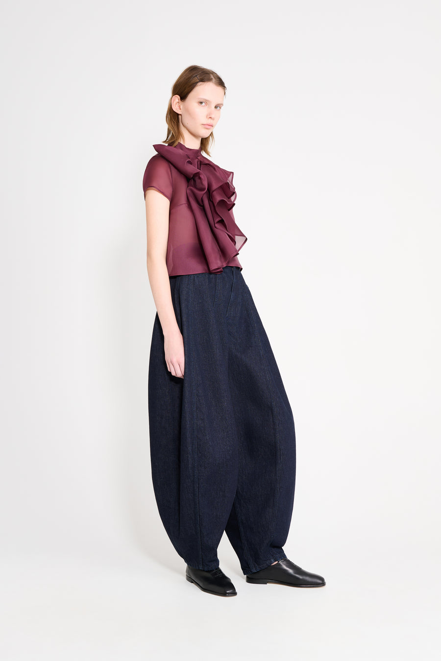 Woman wearing a burgundy top with ruffles and navy blue wide-leg pants on a white background