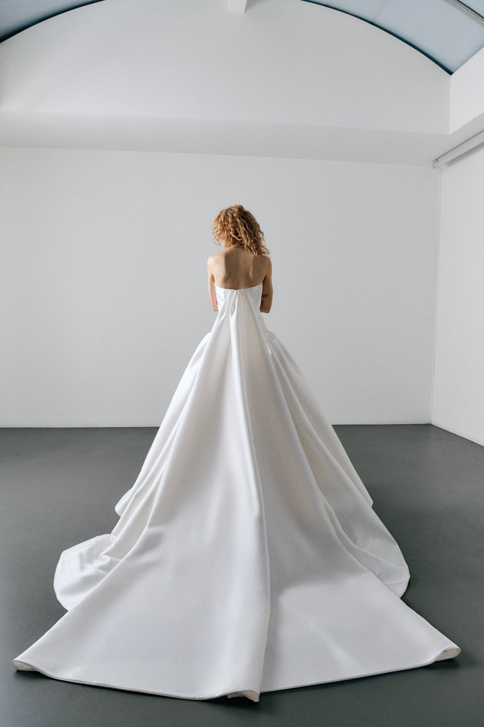 Woman wearing a strapless white wedding dress in a minimalistic room.
