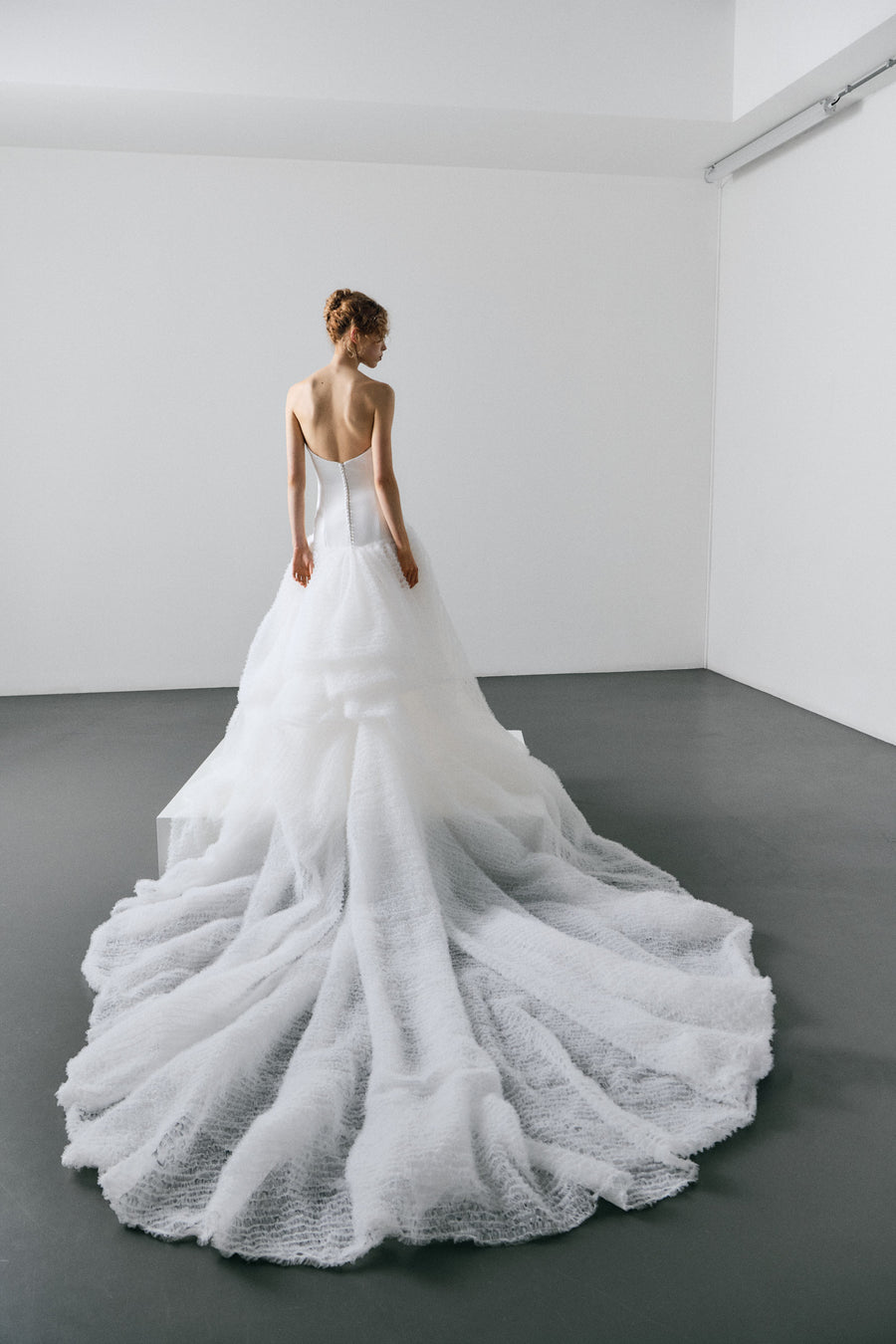 White wedding dress on a model in a minimalistic room with white walls and gray floor.