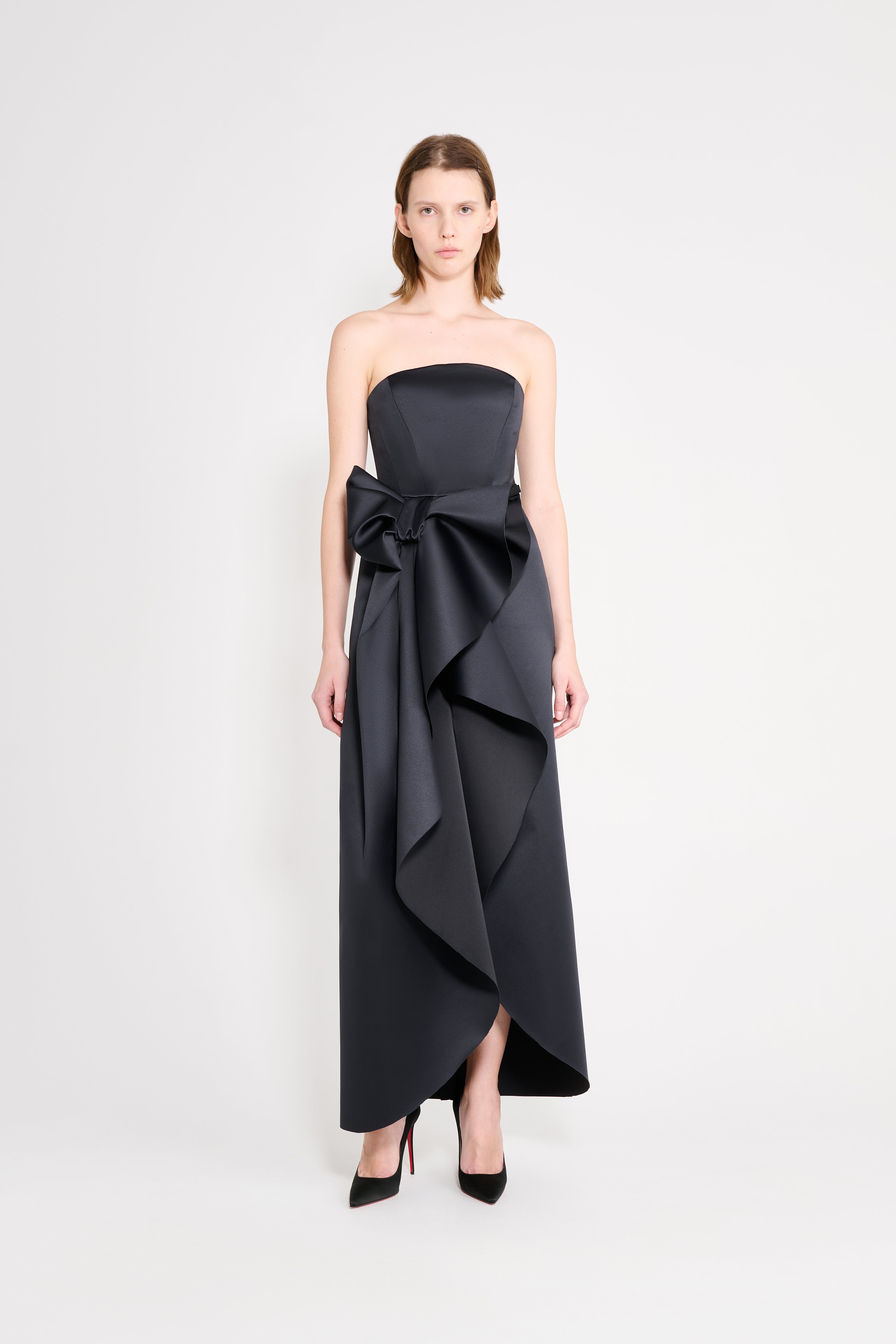 Model wearing a satin black gown with a bow on a white background.