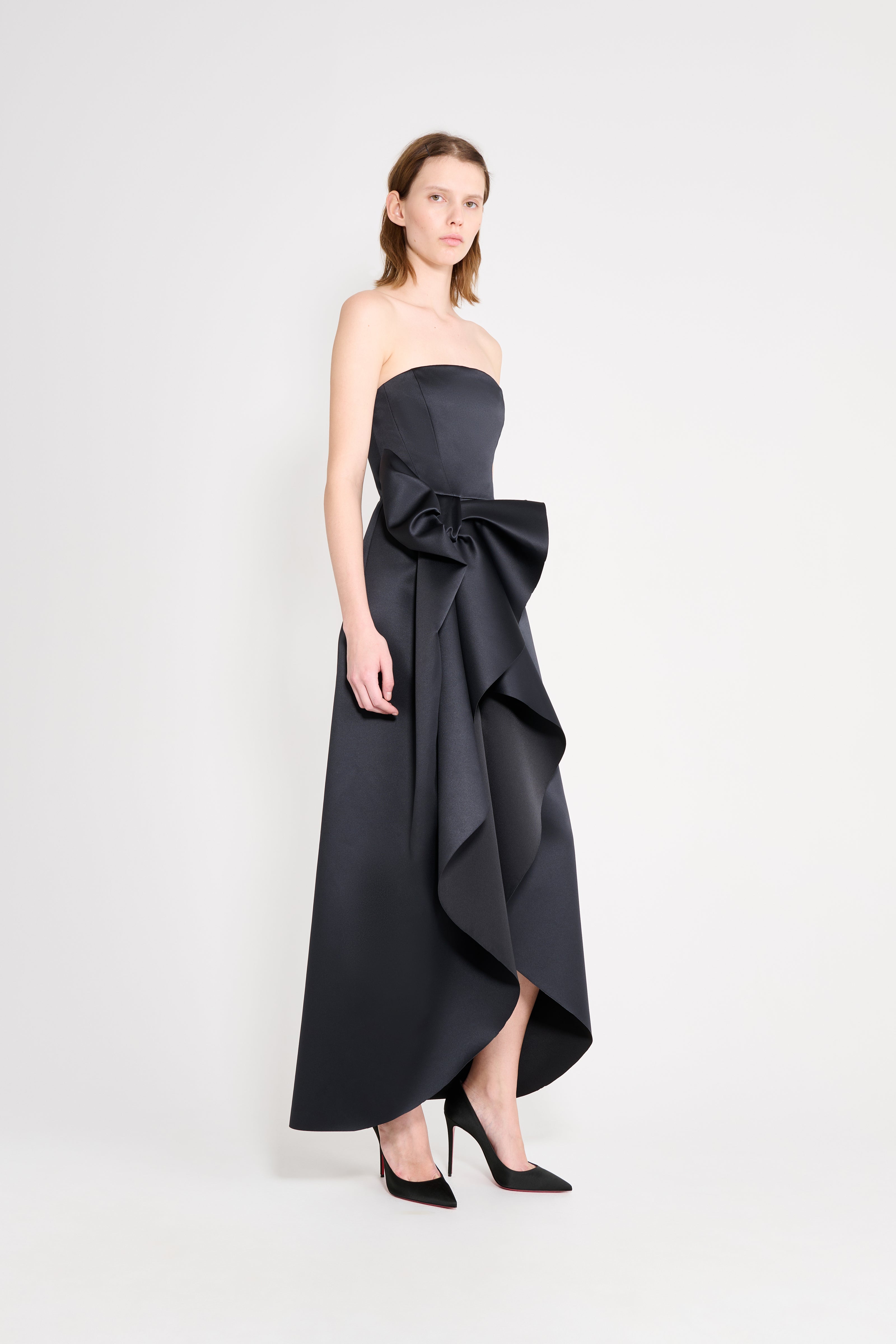 Model wearing a satin black gown with a bow on a white background.