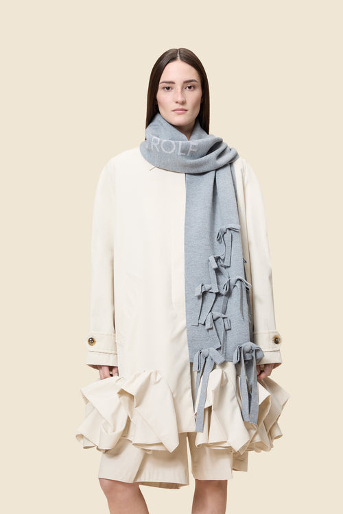 A cream coat with ruffled hem and gold buttons paired with a light gray scarf featuring decorative bows.