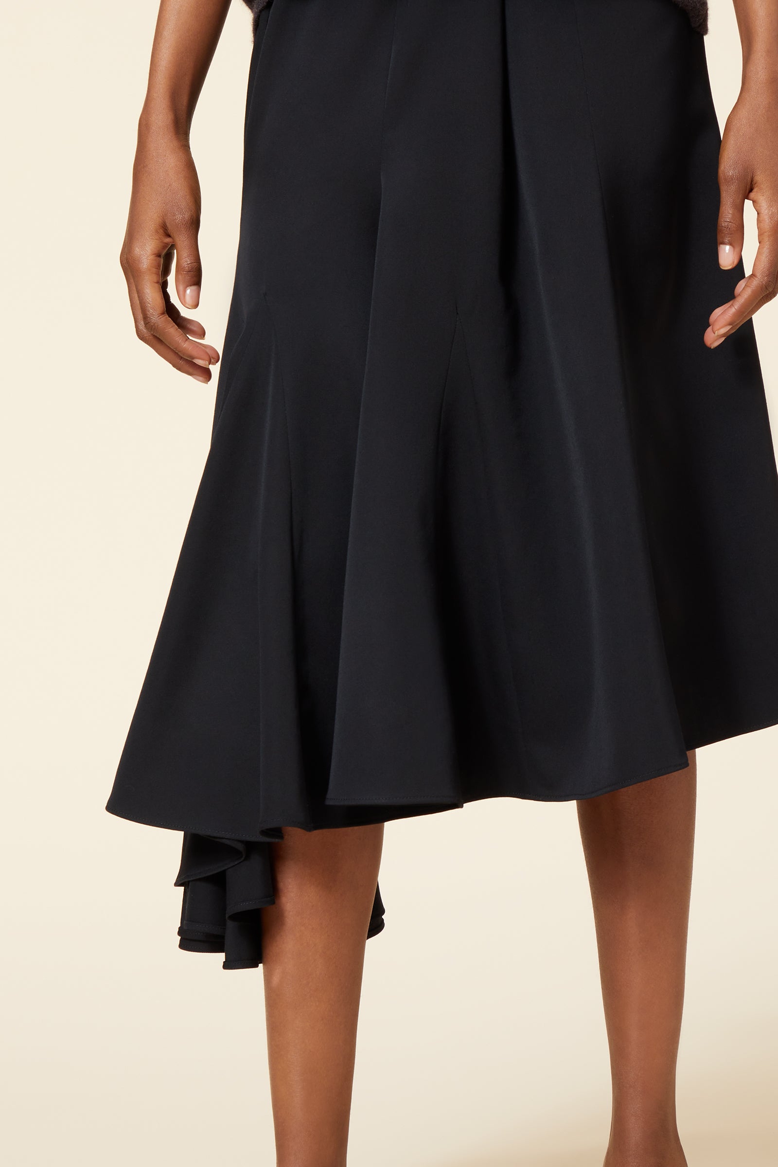 A black satin flared midi skirt featuring asymmetric ruffle detailing, adding elegance and movement to the design.
