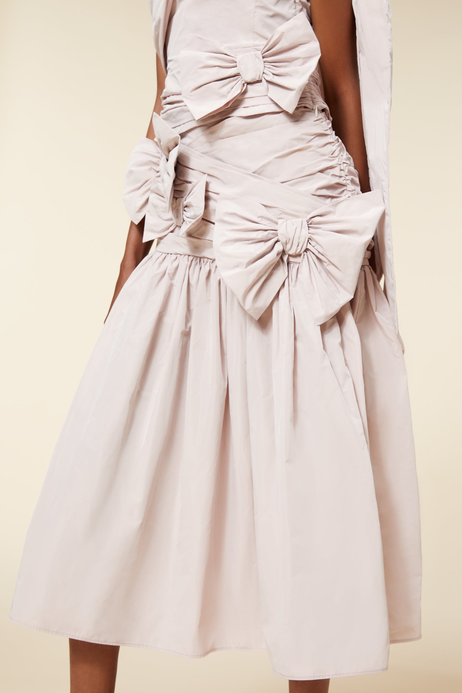 Elegant beige dress with large bow details and ruched fabric, showcasing a chic and sophisticated design.