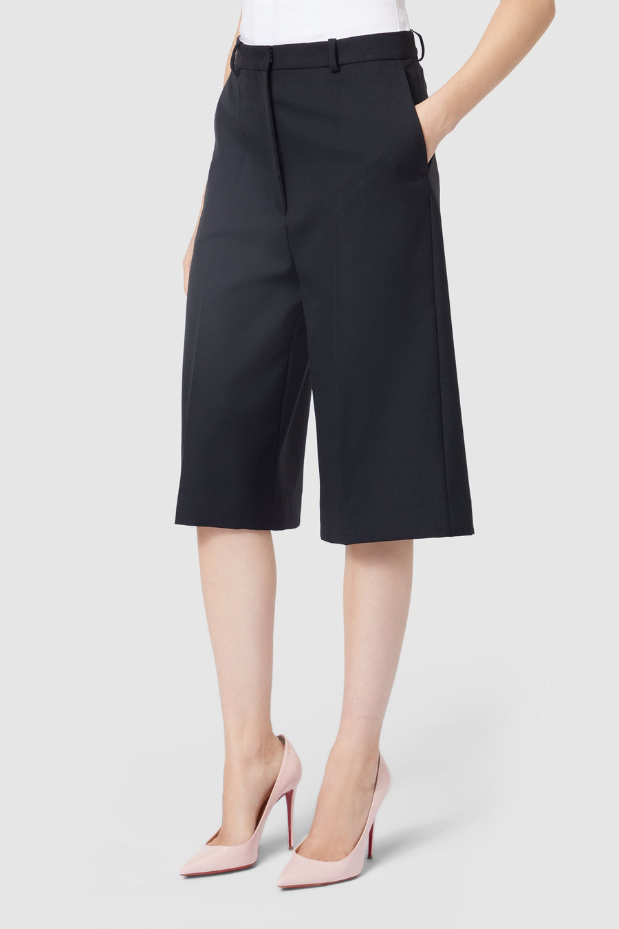 Black tailored culotte shorts with a high waist, featuring side pockets, paired with light pink stiletto heels.