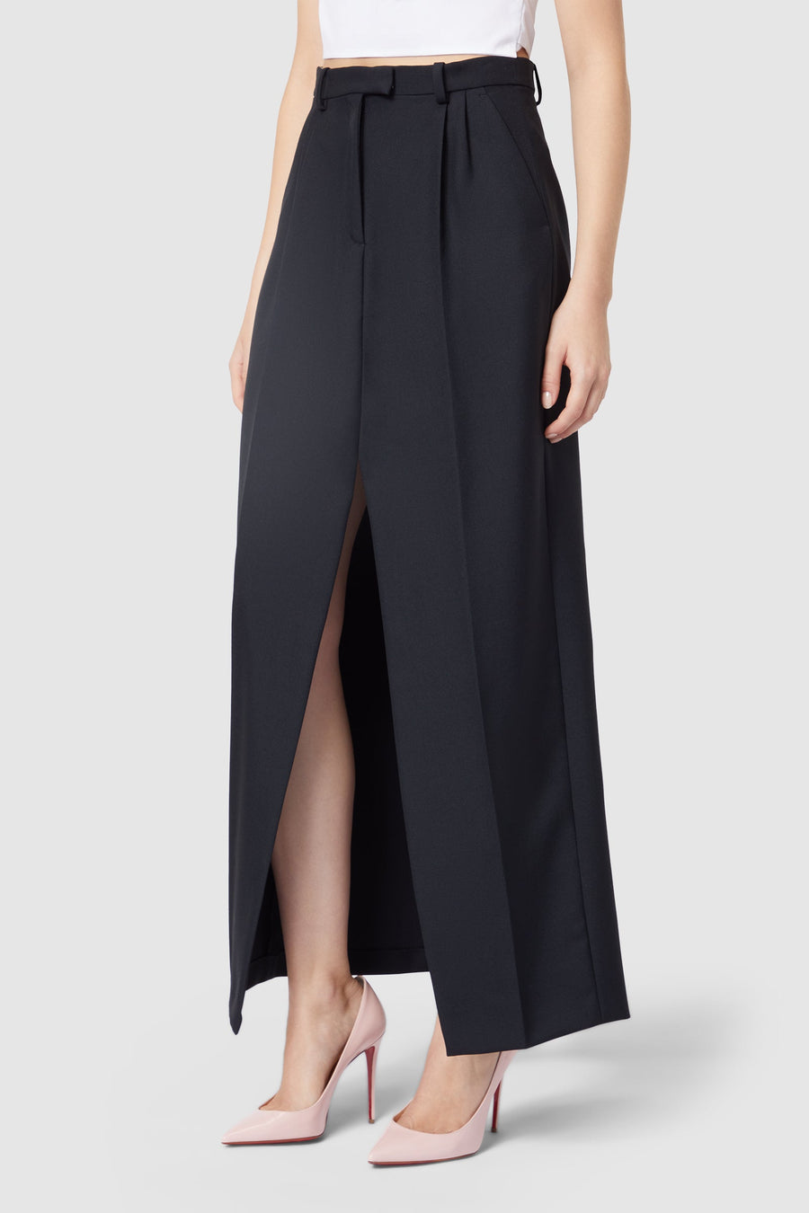 Black high-waisted maxi skirt with front slit detail, paired elegantly with pink stiletto heels and a white top.
