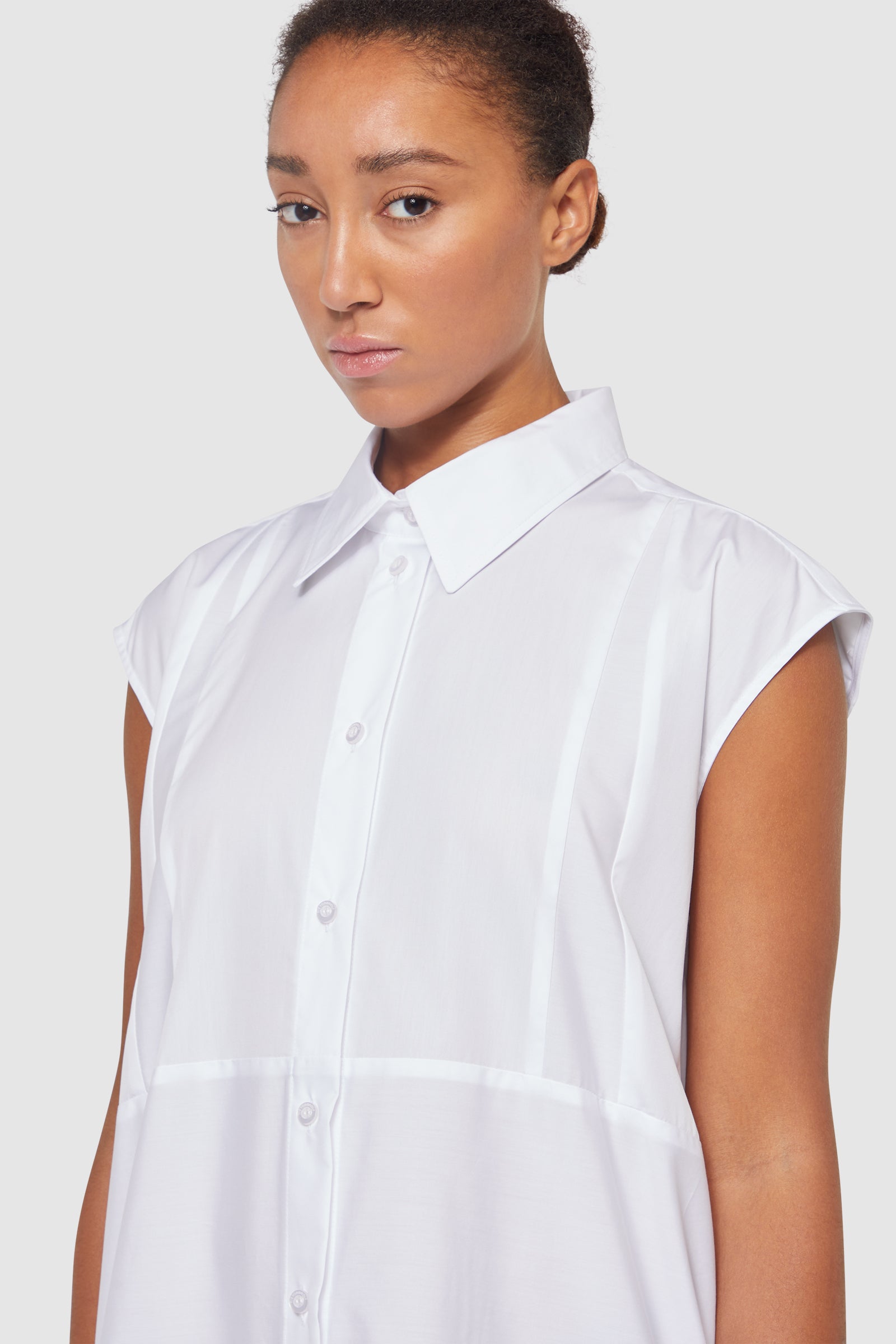 Sleeveless white shirt with crisp collar and button-down front, showcasing minimalist tailoring and elegant design.