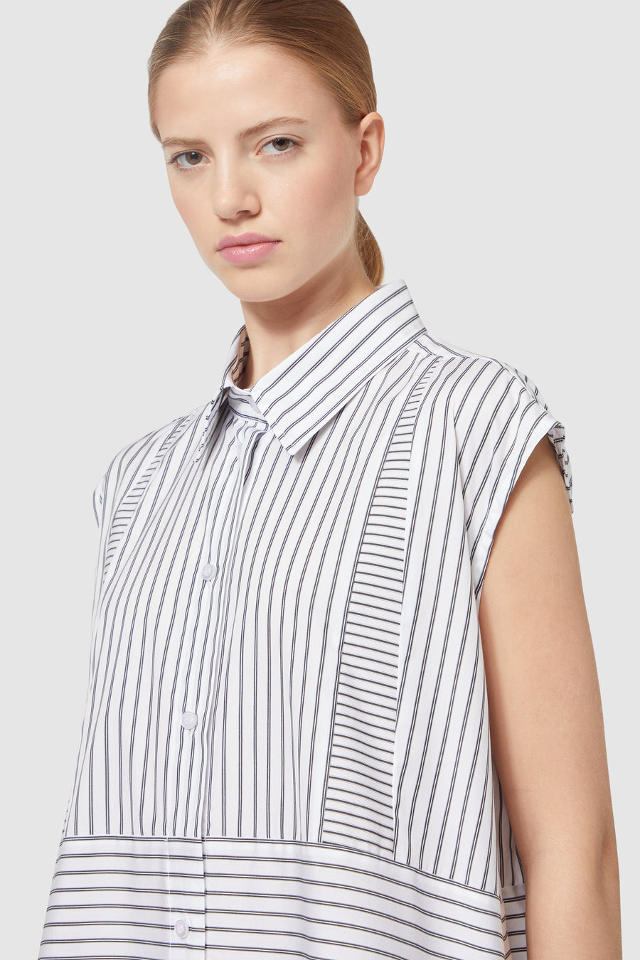 Sleeveless blouse with vertical black and white pinstripes, featuring a classic collar and buttoned front.