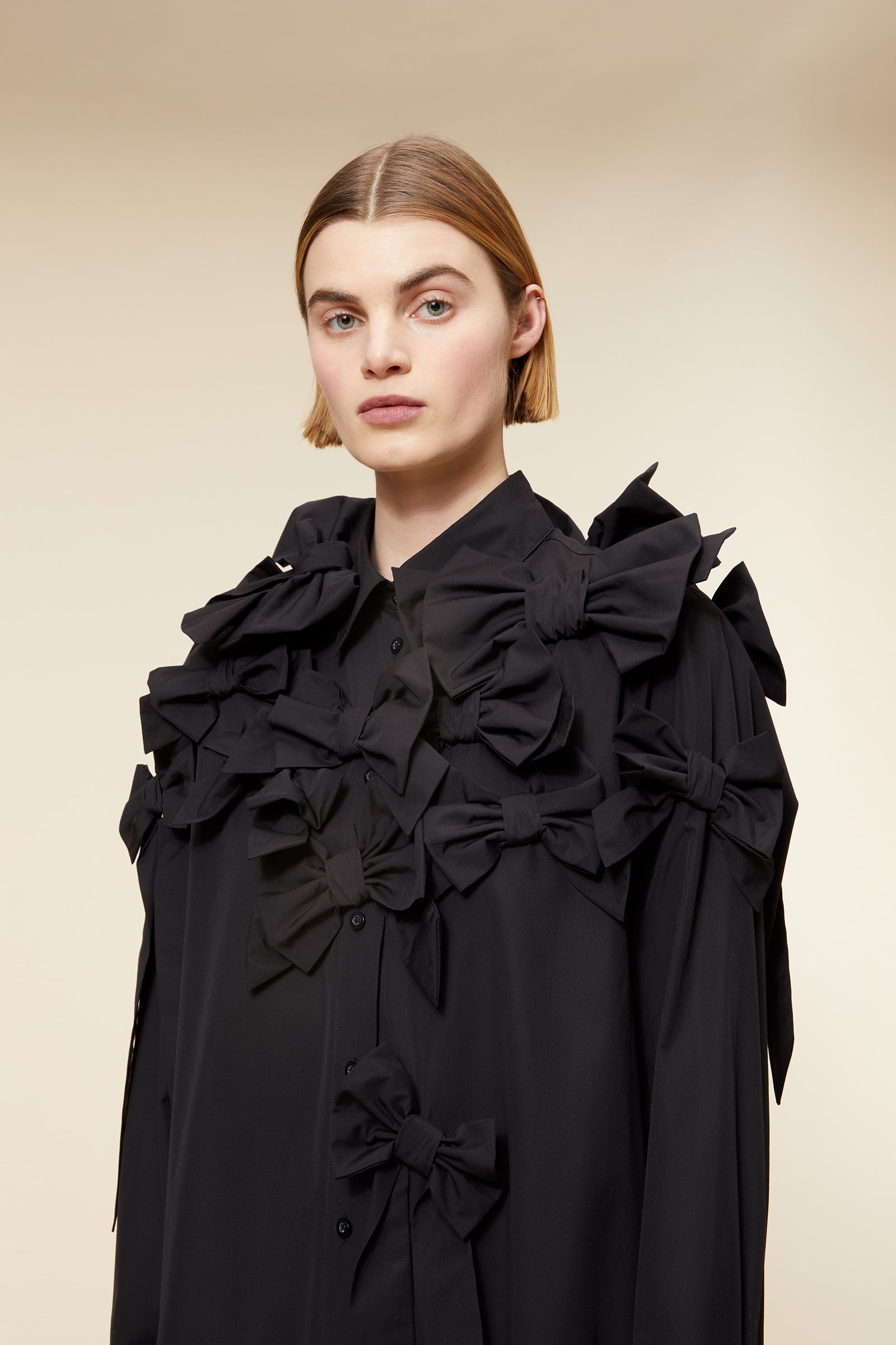 Black shirt dress with intricate ruffle and bow detailing, creating a sophisticated silhouette on a neutral background.