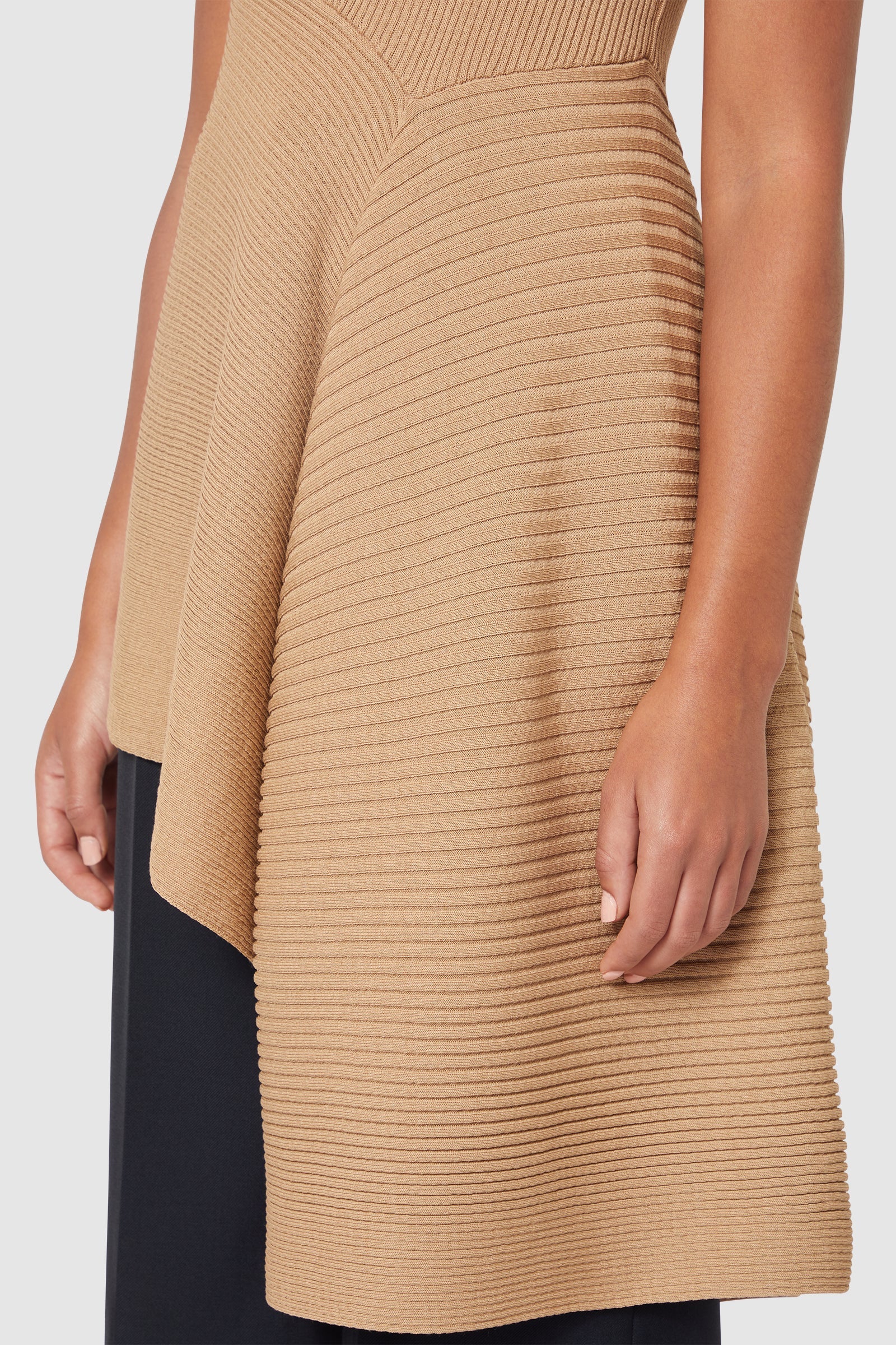 Sleeveless tan knit dress with ribbed texture, featuring an asymmetrical hem and fitted bodice, showcasing elegant draping.
