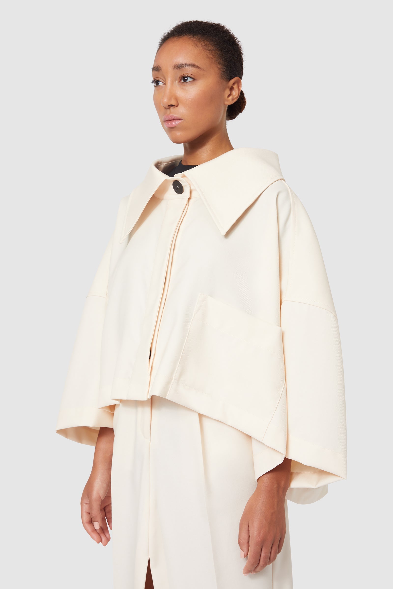 Cream oversized coat with wide collar and single black button closure, featuring minimalist oversized front pockets.