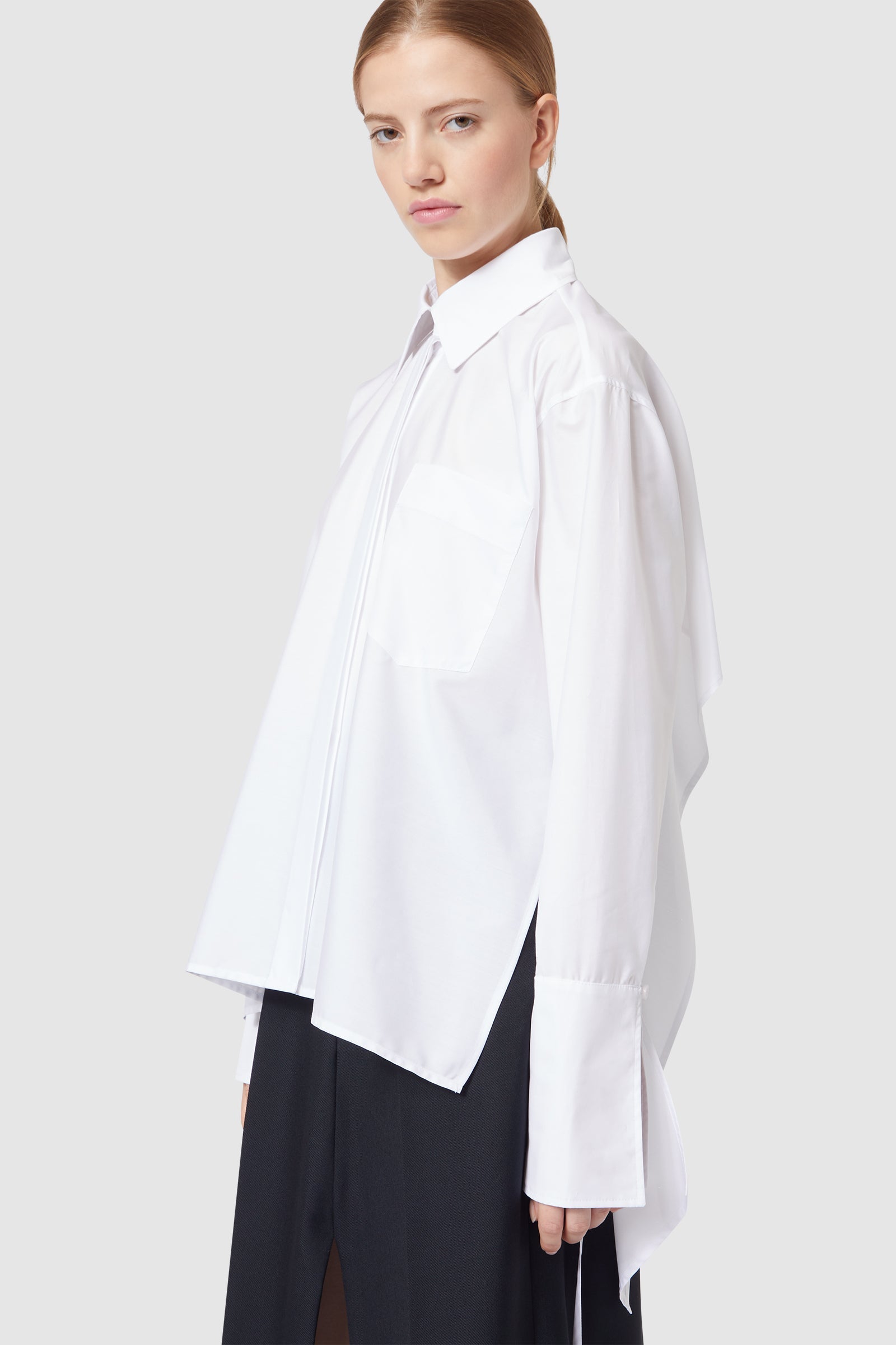 White long-sleeved shirt with oversized cuffs and subtle design details, worn over wide-leg black pants.