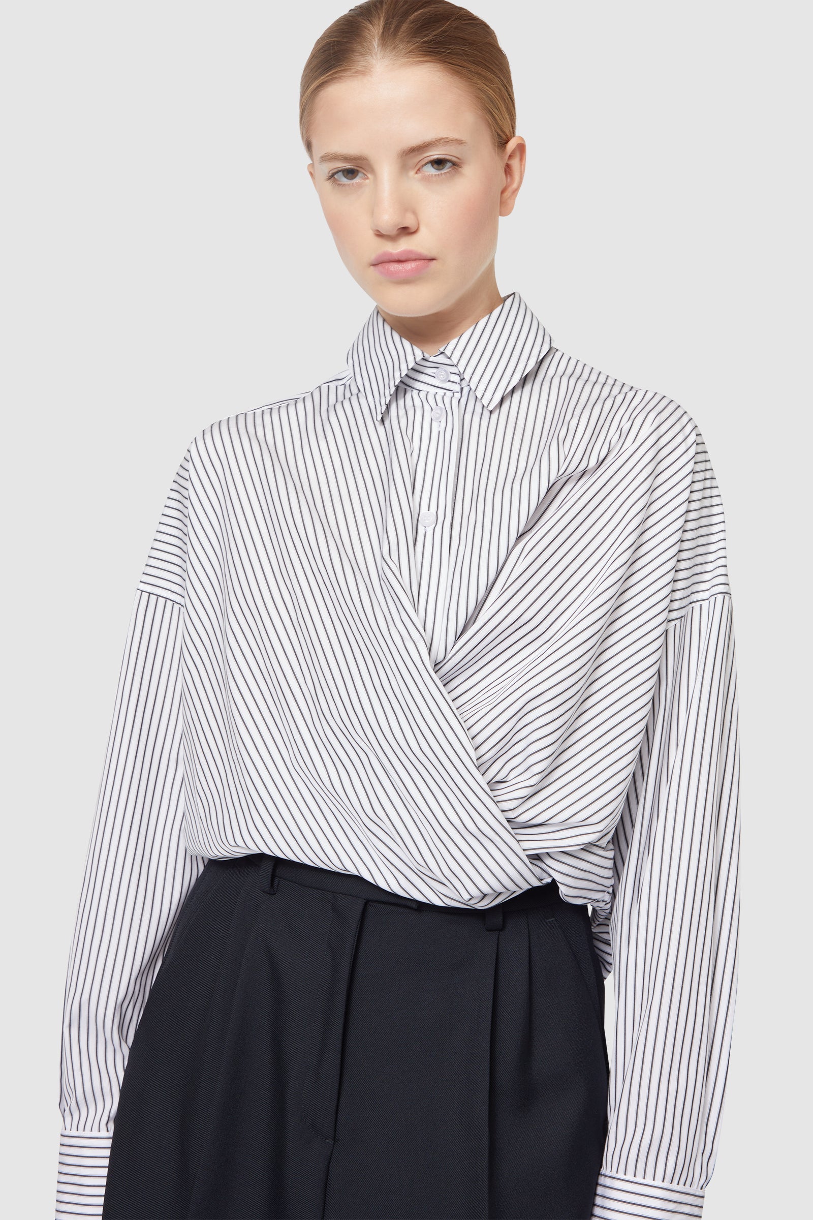 A tailored pinstripe wrap blouse elegantly paired with high-waisted black trousers, showcasing minimalist chic fashion.