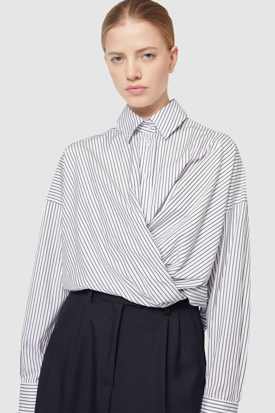 A tailored pinstripe wrap blouse elegantly paired with high-waisted black trousers, showcasing minimalist chic fashion.