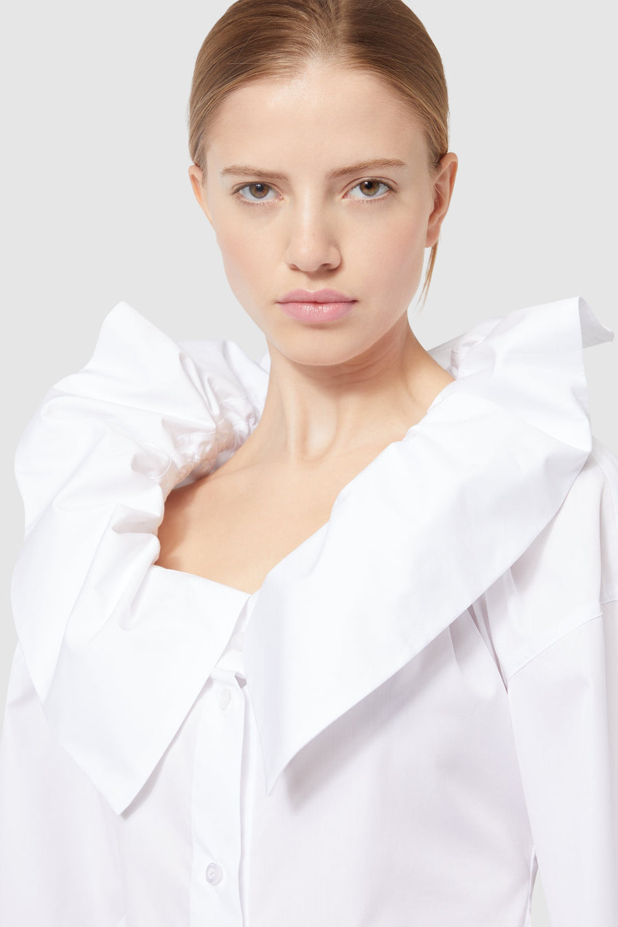 White blouse with a large ruffled collar, styled elegantly for a modern and sophisticated look.