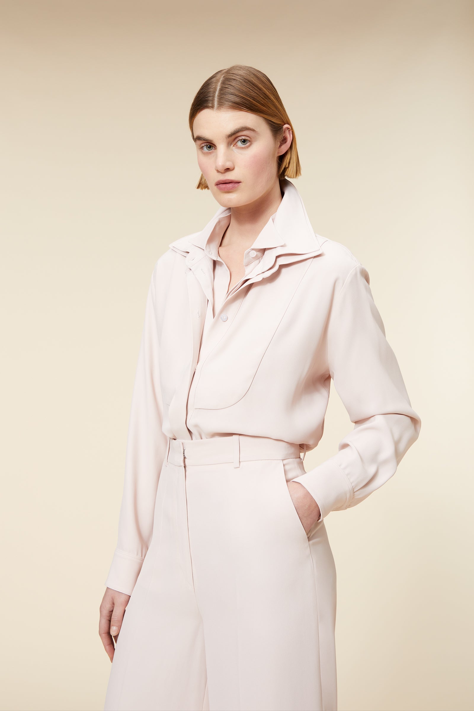 Woman wearing a light beige jumpsuit with wide-leg pants, collared neckline, and button-up front on a neutral background.