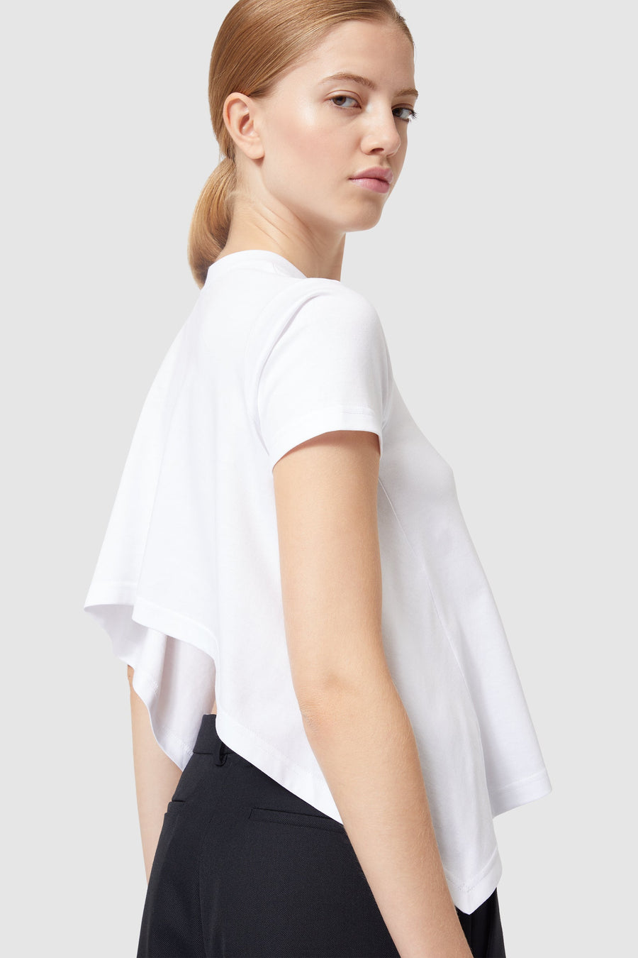 White asymmetric cotton-blend t-shirt with a unique draped back design paired with sleek black trousers.