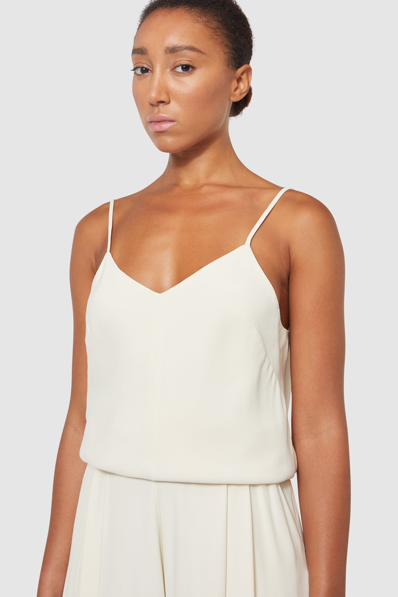 Sleek cream satin dress with delicate spaghetti straps, featuring a fitted bodice and subtle pleated detailing for elegant movement.