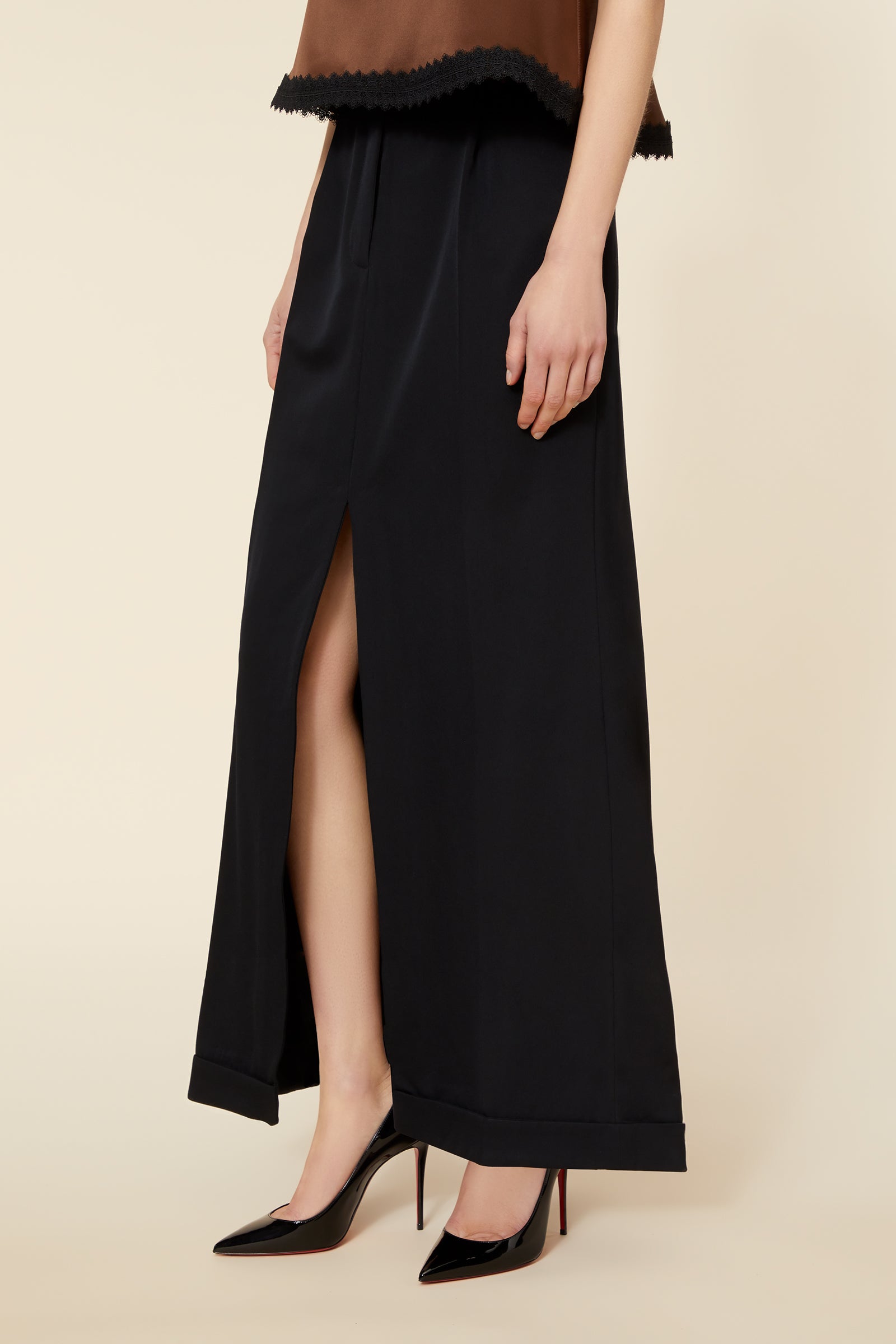 Black maxi skirt features a sleek high slit, paired with brown top, complemented by black patent high-heeled shoes.