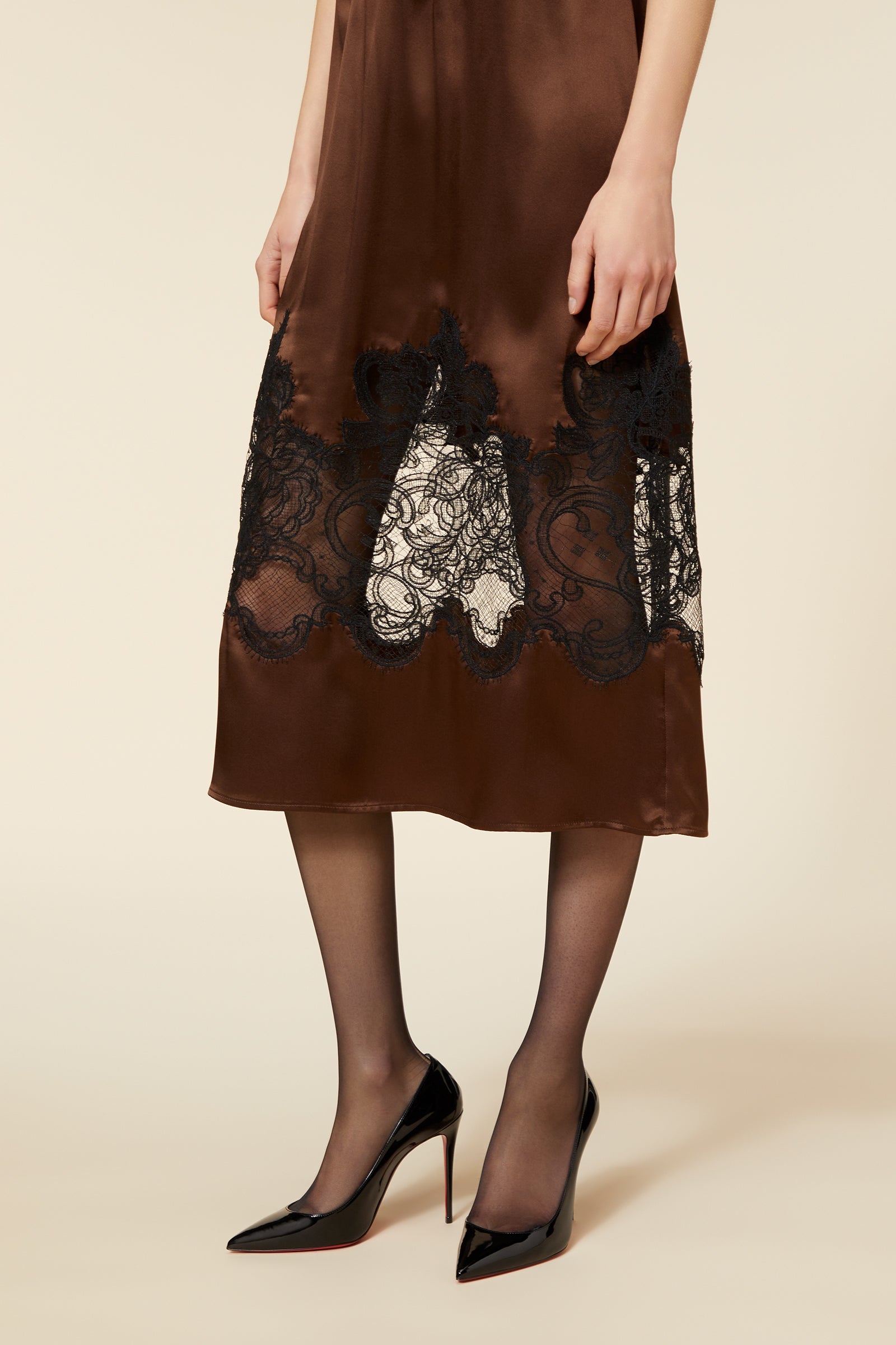 Silk brown dress with intricate black lace detailing at the hem, paired with sheer stockings and black patent heels.