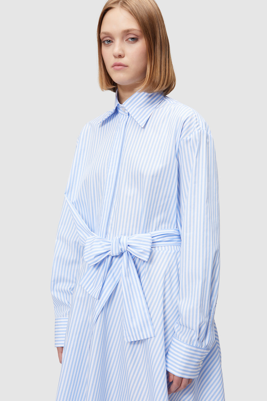 Striped button-up dress in soft blue and white with a matching tie waist belt, featuring a classic collar design.