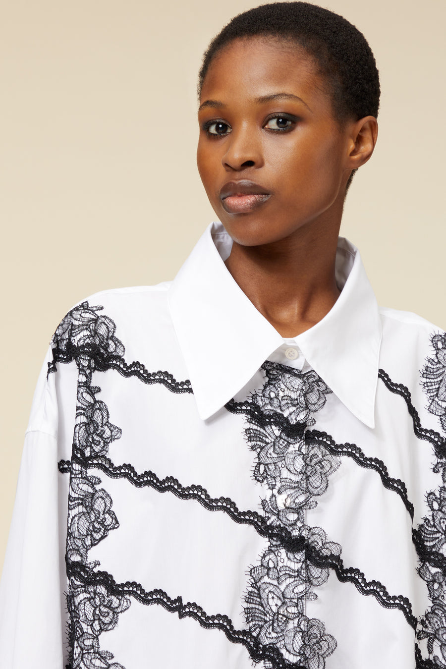 White shirt with intricate black lace detailing, featuring a wide collar and artistic floral patterns on the fabric.