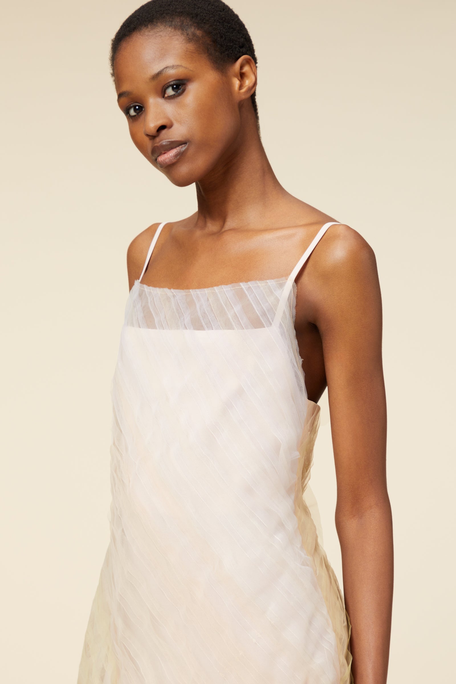 Model wearing a light pastel-colored, sleeveless dress with thin straps and subtle geometric patterns.