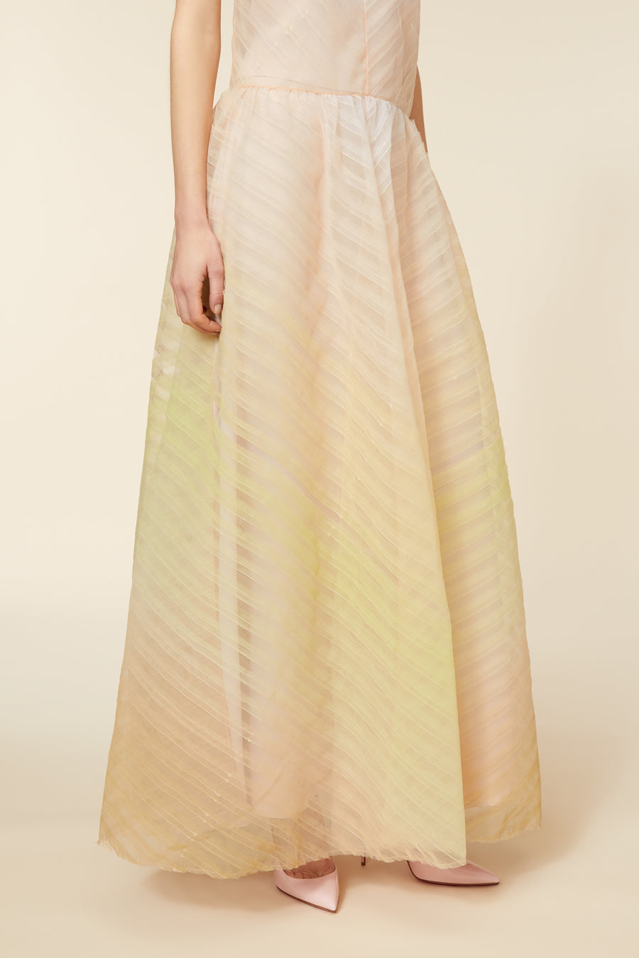 Elegant pastel flowing gown with subtle diagonal patterns and soft pink heels, highlighting delicate evening attire.