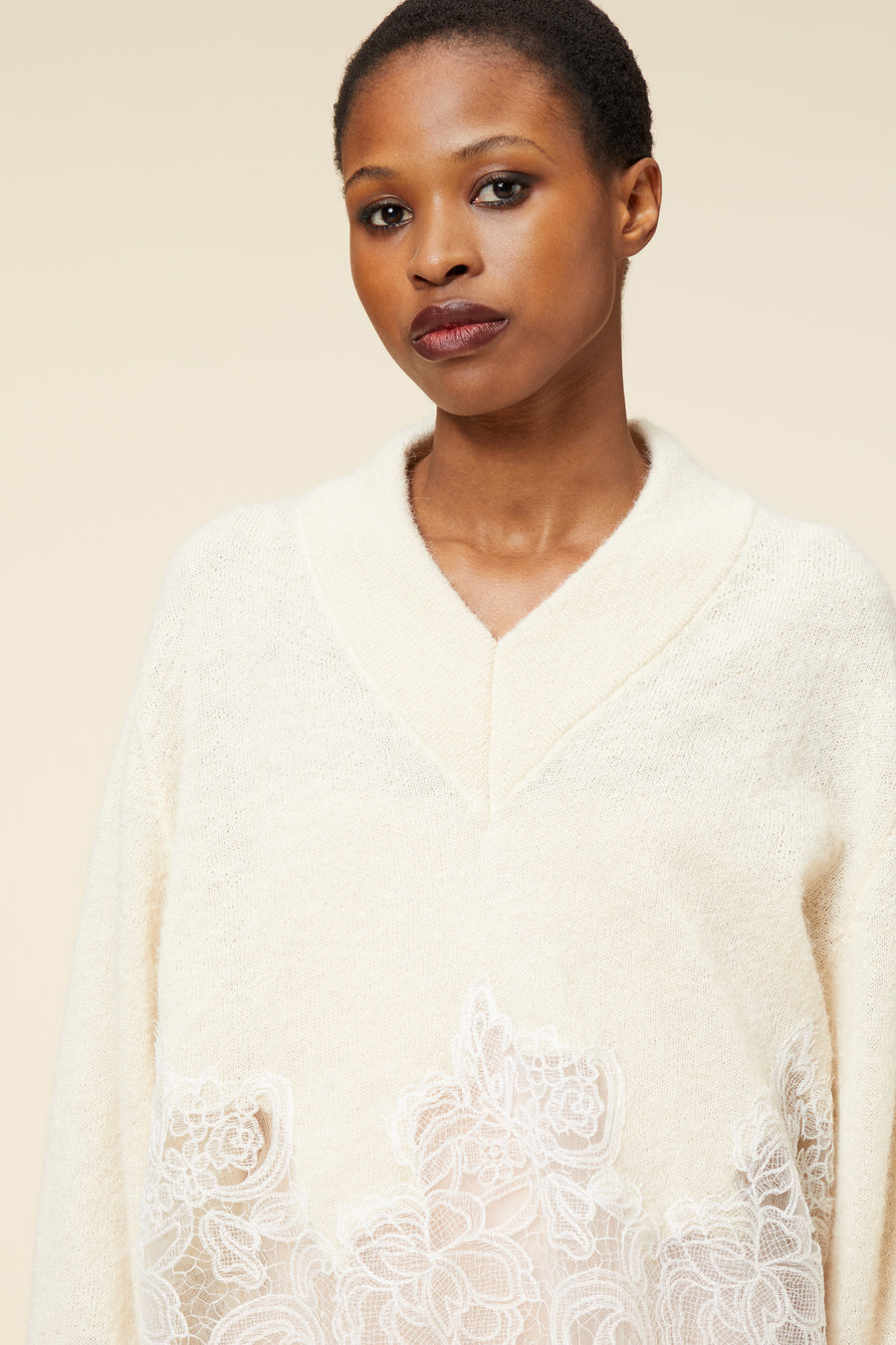 Cream knit sweater with a wide collar and intricate floral lace appliqué detailing at the hem, adding a touch of elegance.