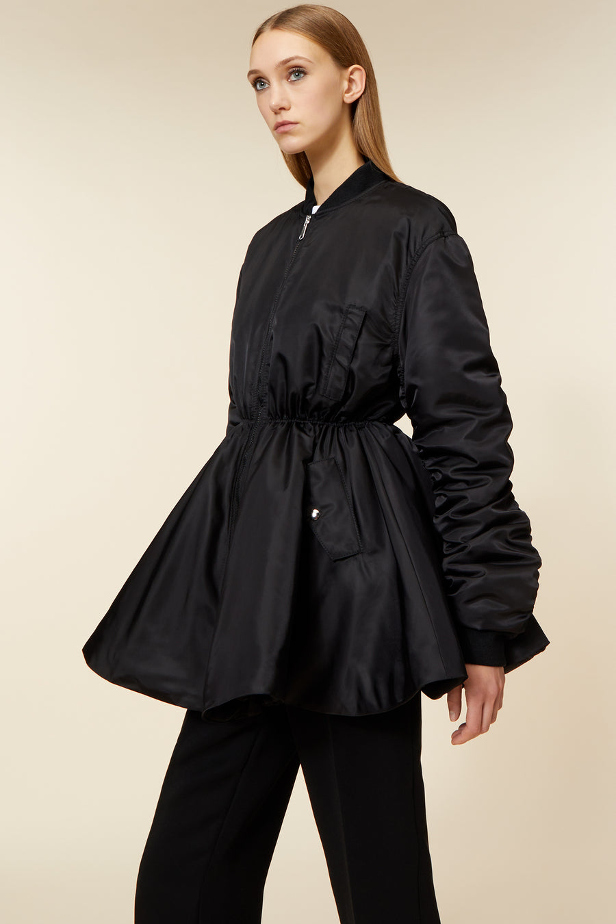 Elegant black satin bomber jacket with flared waist and elastic drawstring detail, paired with tailored black pants.