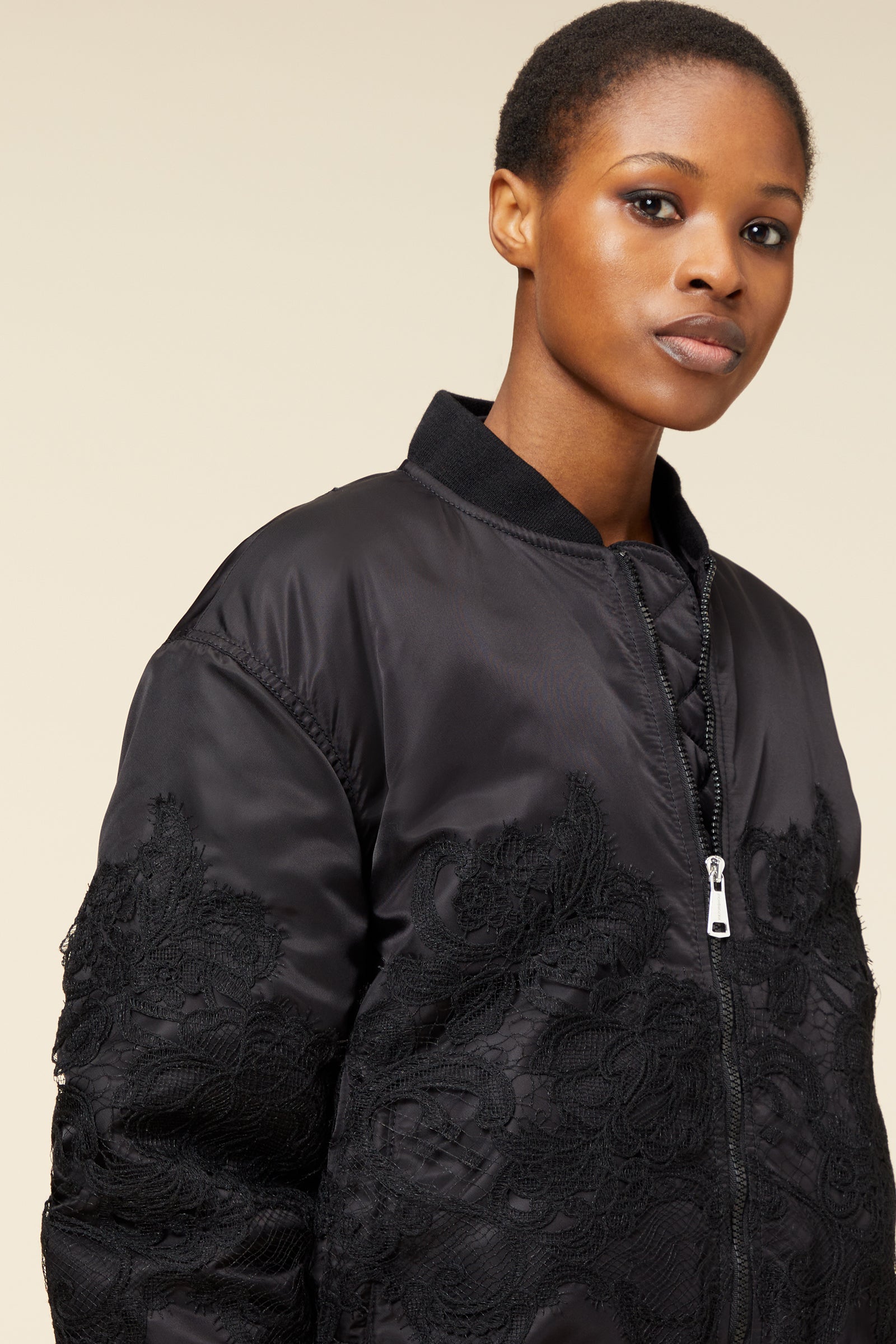 Black bomber jacket featuring intricate lace detailing on the sleeves, with a sleek zipper closure and ribbed collar.