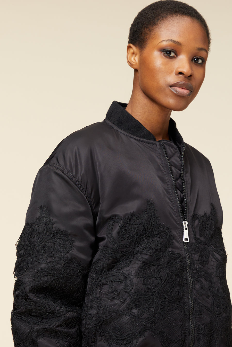Black bomber jacket featuring intricate lace detailing on the sleeves, with a sleek zipper closure and ribbed collar.