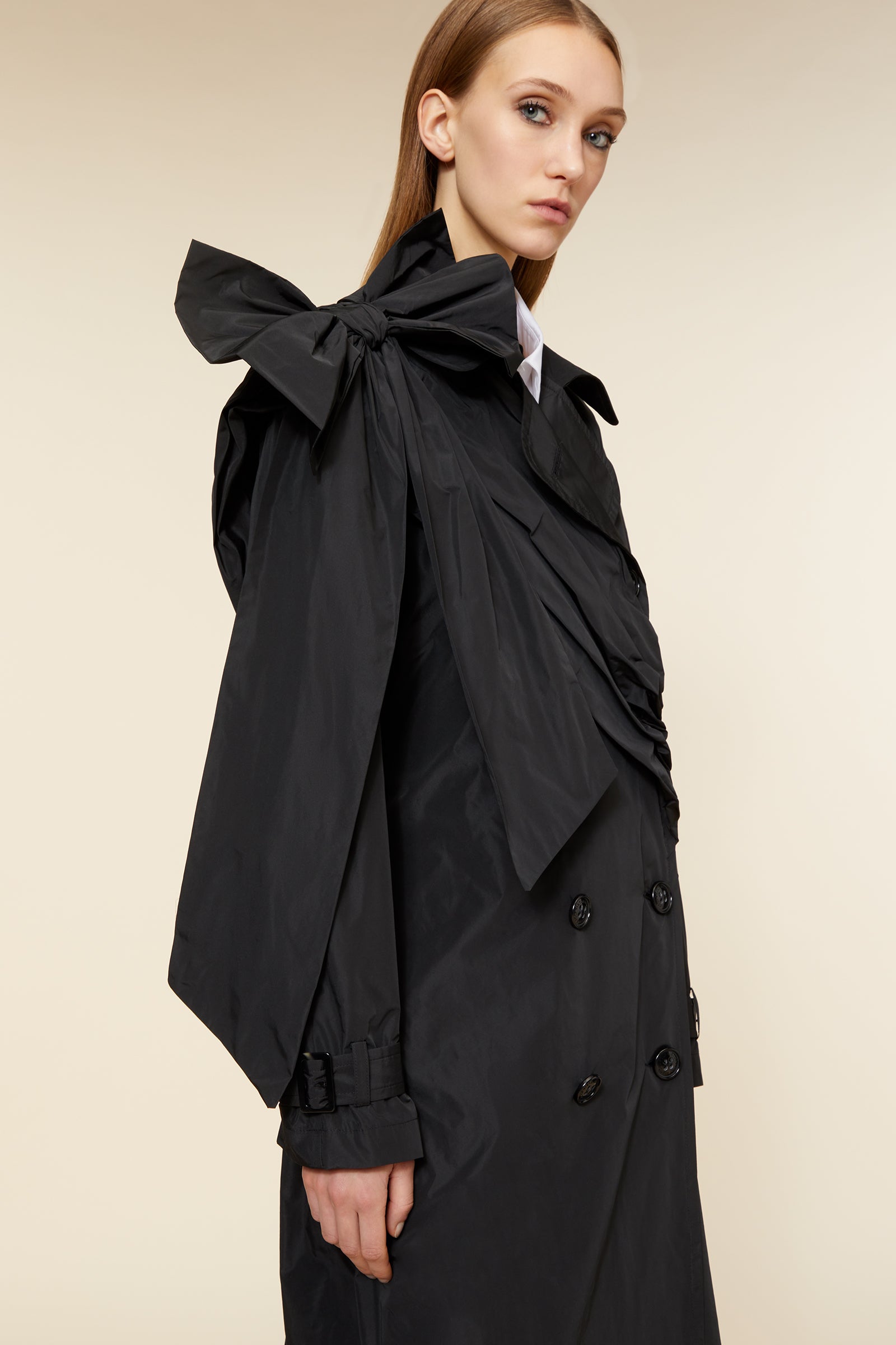 Luxurious black trench coat featuring oversized bow on the shoulder, double-breasted front, and sleek, tailored fit.