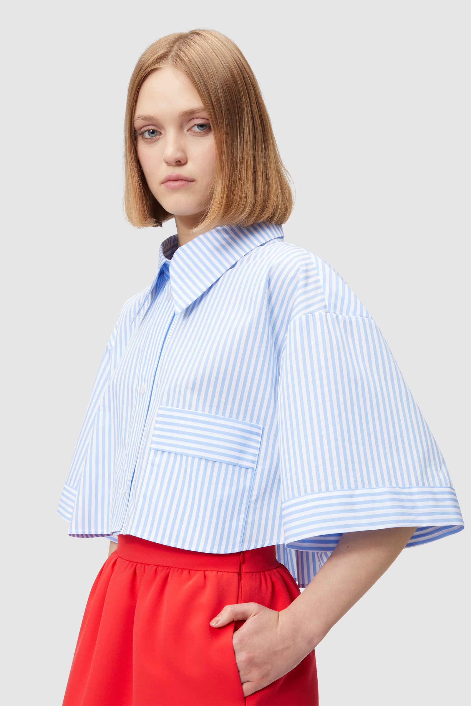 A blue and white striped oversized shirt with wide sleeves paired with vibrant red high-waisted skirt.