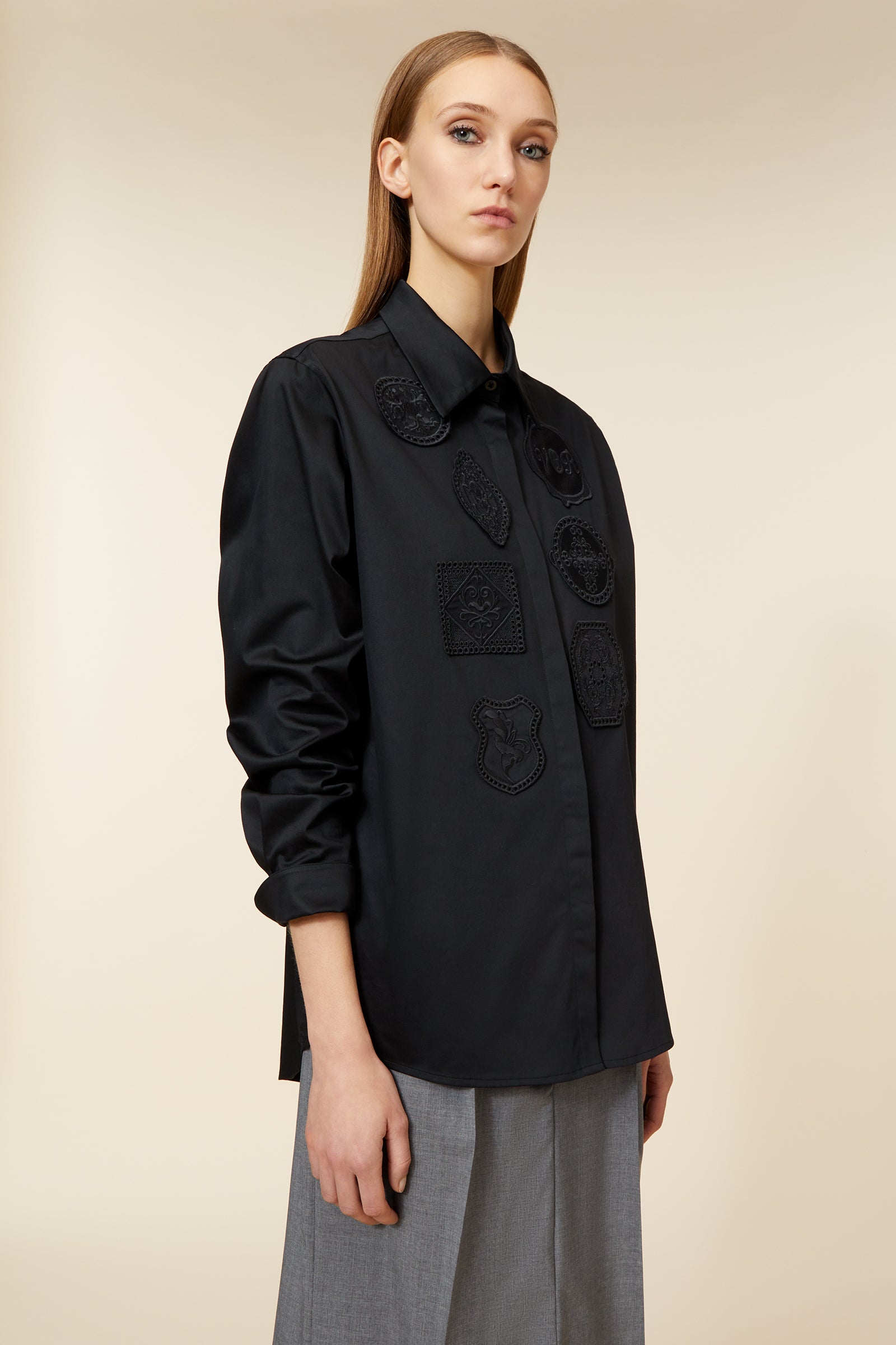 Elegant black shirt with intricate patch designs paired with tailored gray trousers, showcasing a minimalist fashion style.