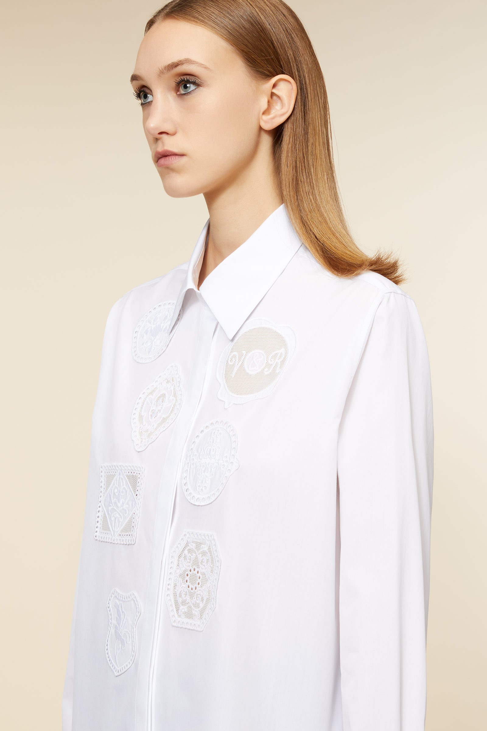 Elegant white shirt with intricate embroidered lace patches, featuring a classic collar and sleek silhouette.