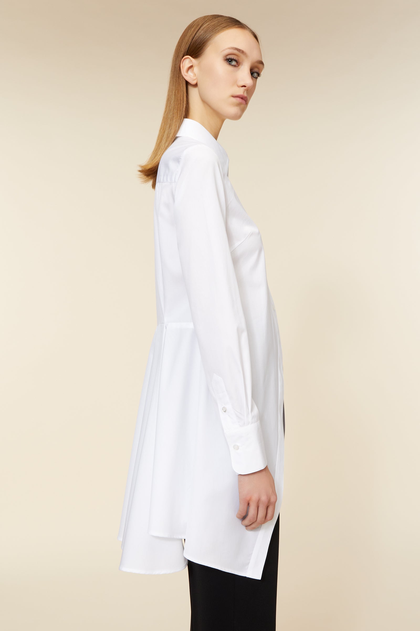 A white longline shirt with classic collar and buttoned cuffs, expertly tailored for a sleek, minimalist silhouette.