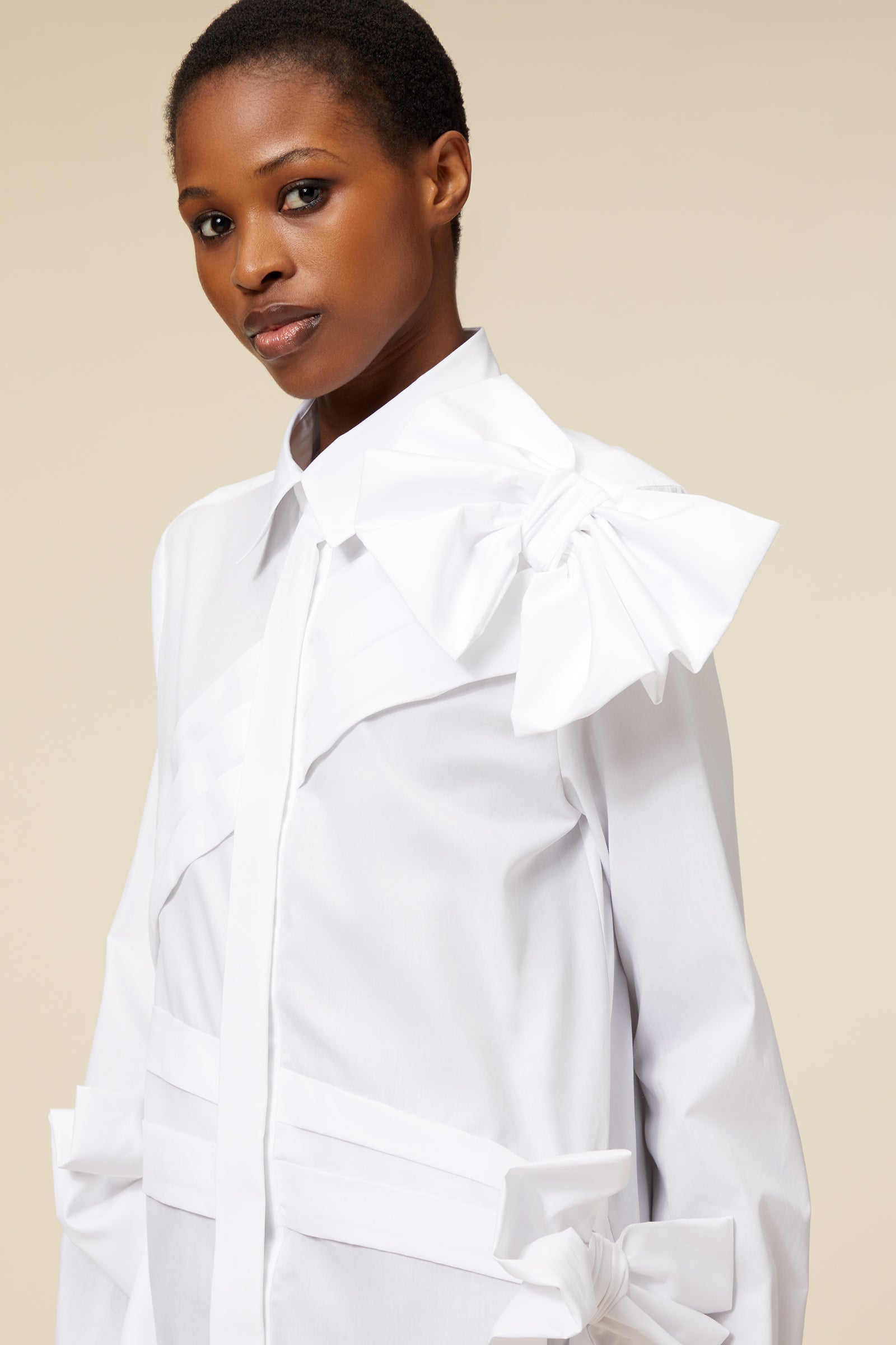 White tailored shirt with decorative bow on shoulder, featuring sleek design elements and crisp material texture.