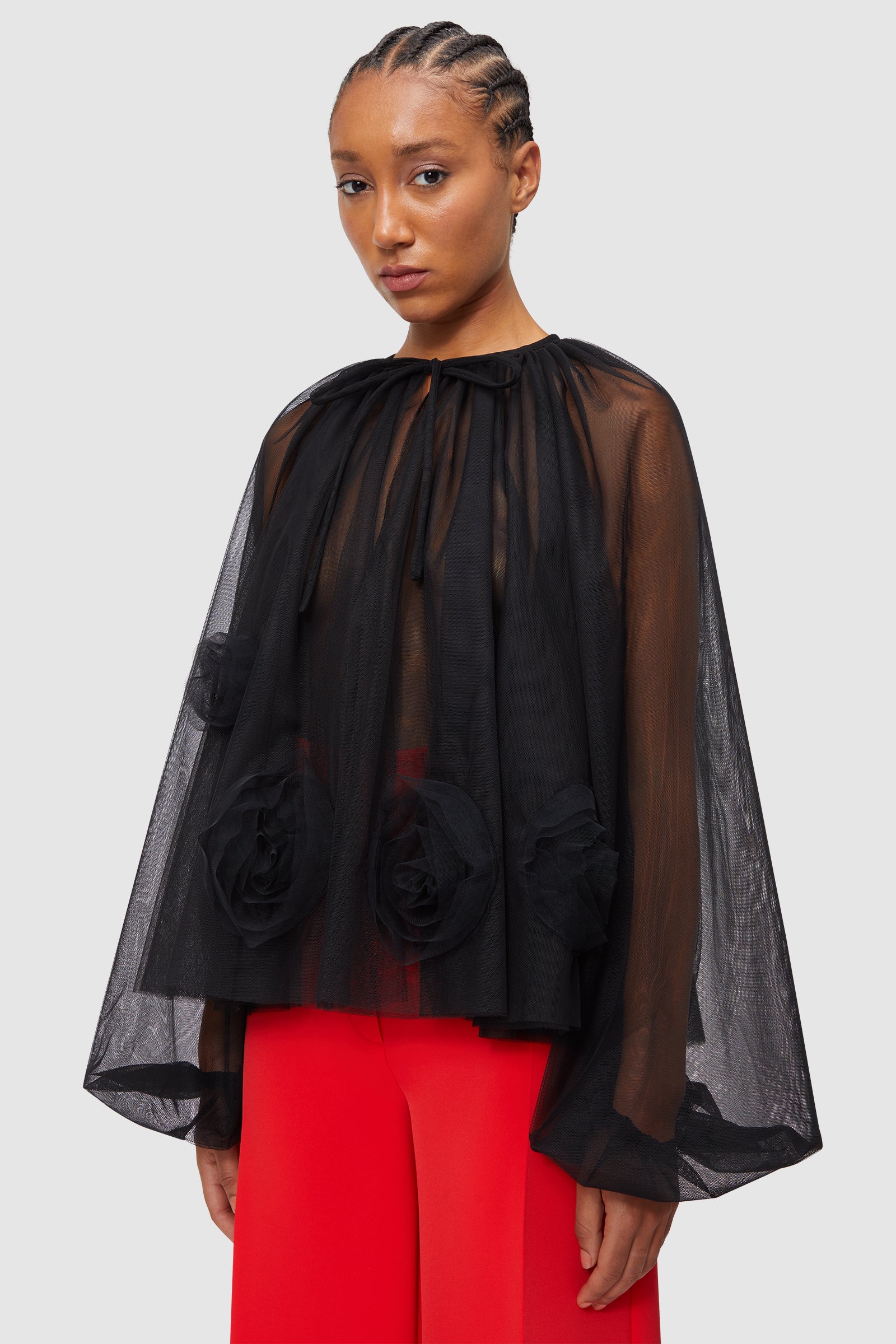 Black sheer tulle top with voluminous sleeves and large rose applique detailing, paired with vibrant red trousers.