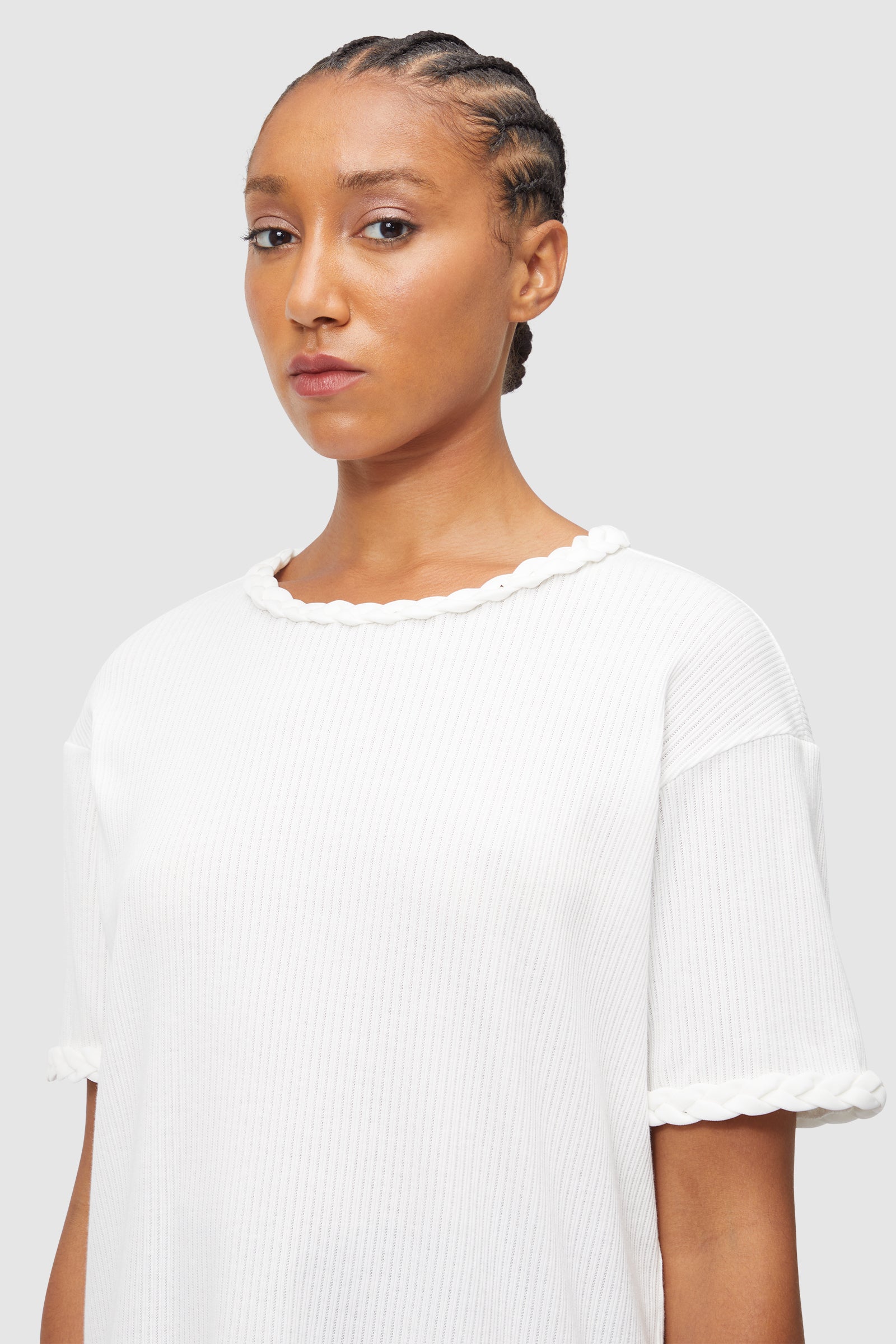 A white ribbed knit top features elegant braided trim accents on the neckline and sleeves, adding subtle sophistication.
